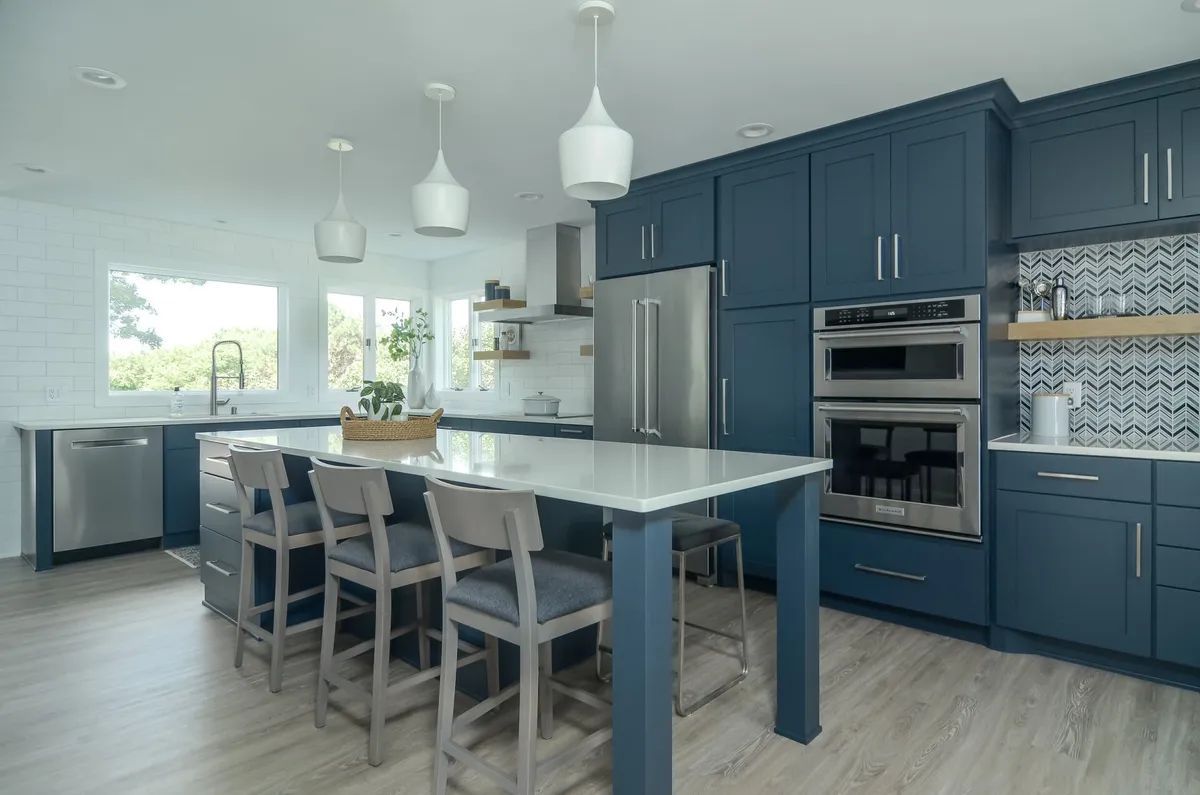 Modern kitchen with navy cabinets, island, bar stools, stainless appliances, and white pendant lights