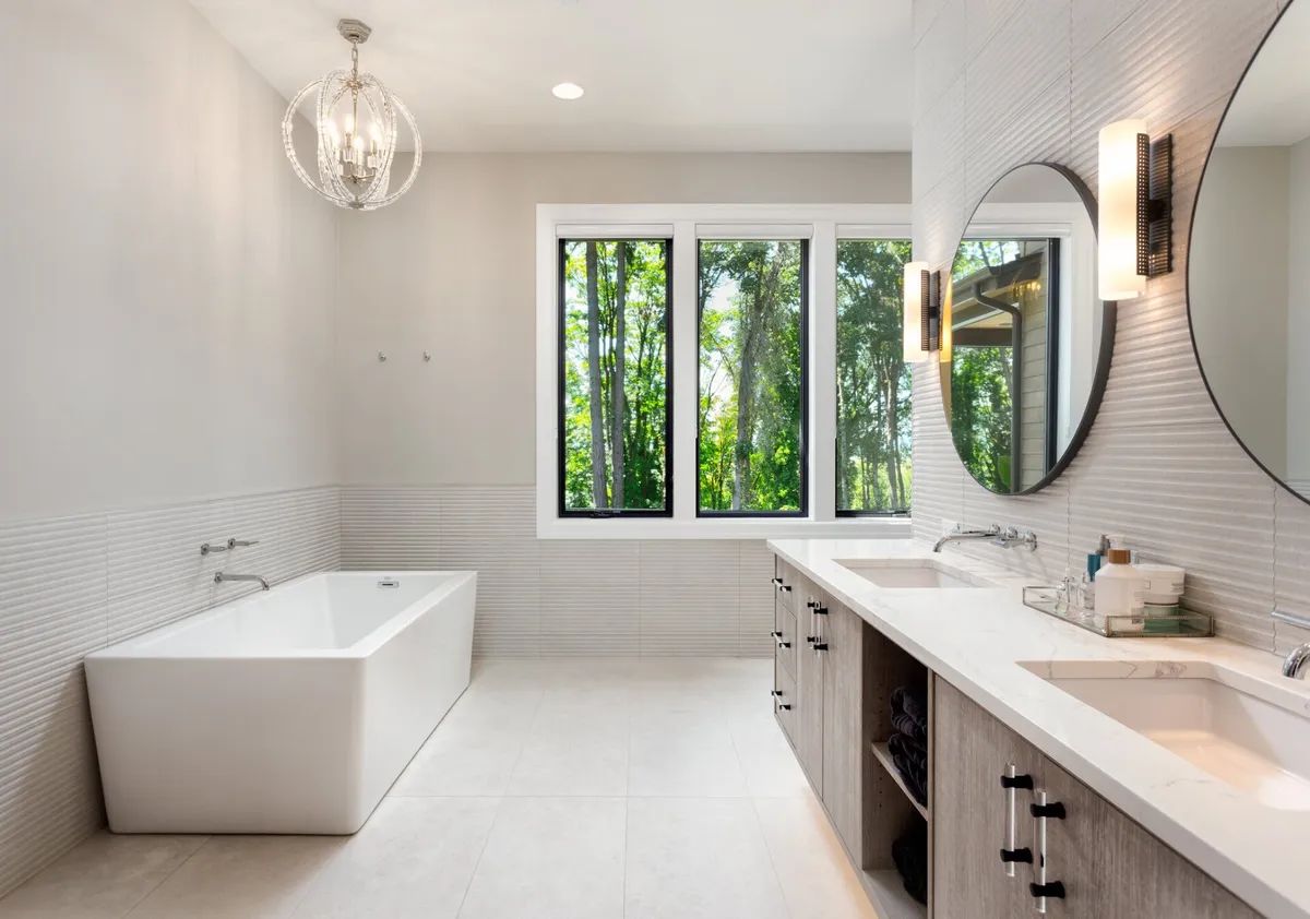 A bathroom with a tub , sinks , mirrors and a large window.