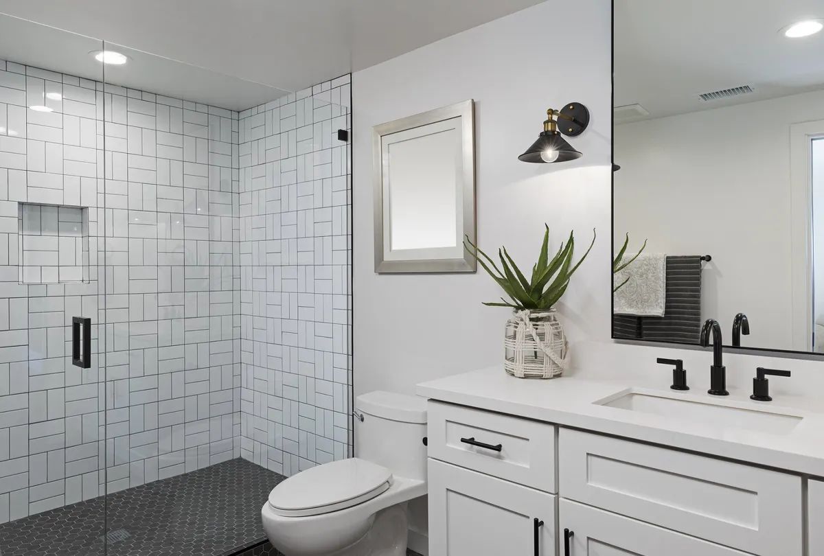 A bathroom with a toilet , sink , mirror and walk in shower.
