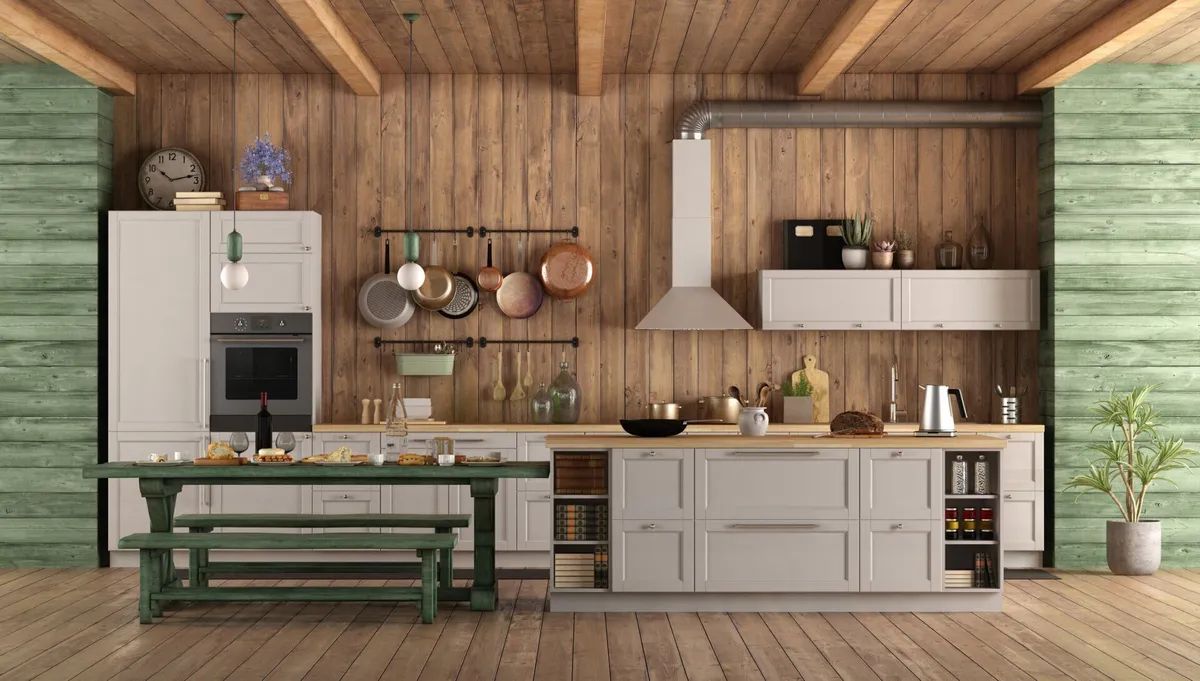 A kitchen with wooden walls , white cabinets , a table and benches.