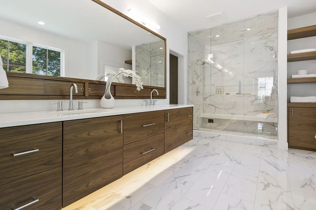 Modern bathroom with dark wood vanity, white marble tile, large mirror, and glass shower enclosure