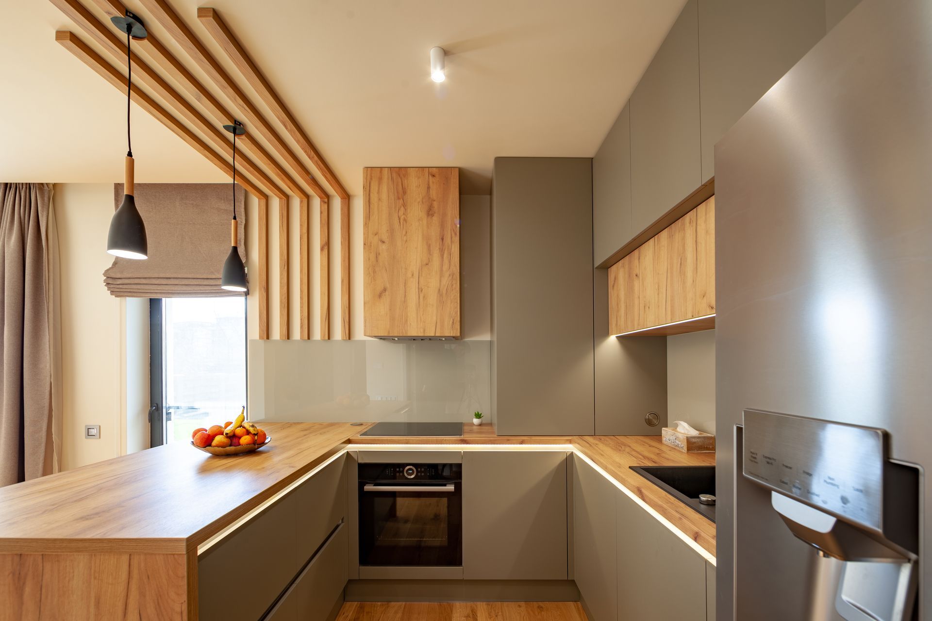 Modern kitchen with wood accents, gray cabinets, hanging pendant lights, and a fruit bowl on the island