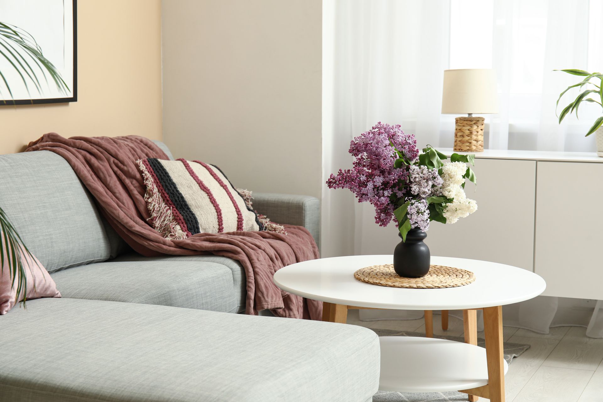 Cozy living room with gray sofa, striped throw, round white table, and purple flowers in a vase