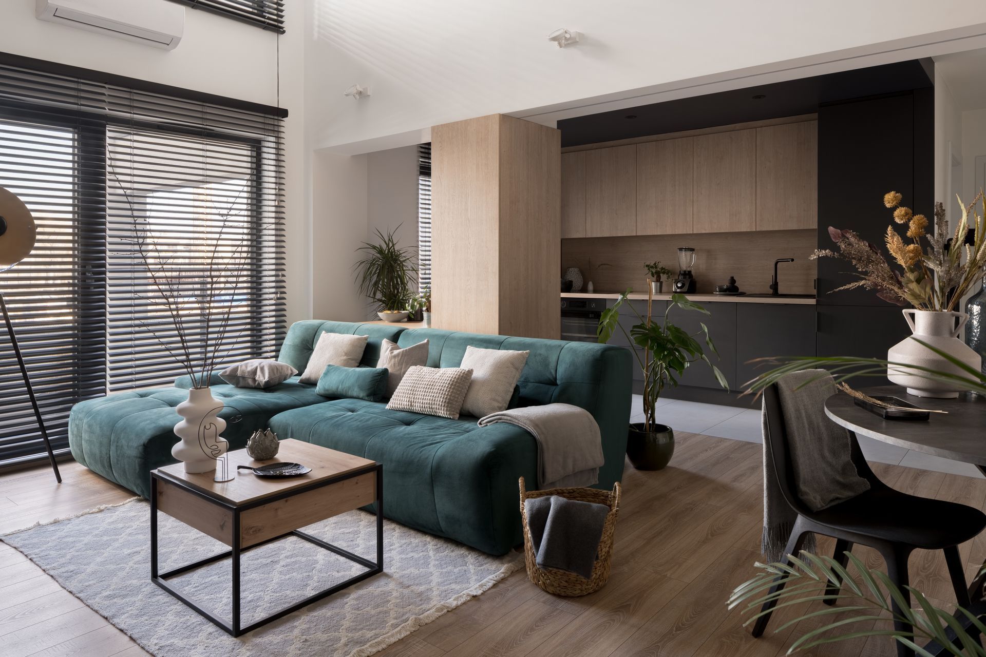 Modern living room with teal sofa, coffee table, armchair, and open kitchen in the background