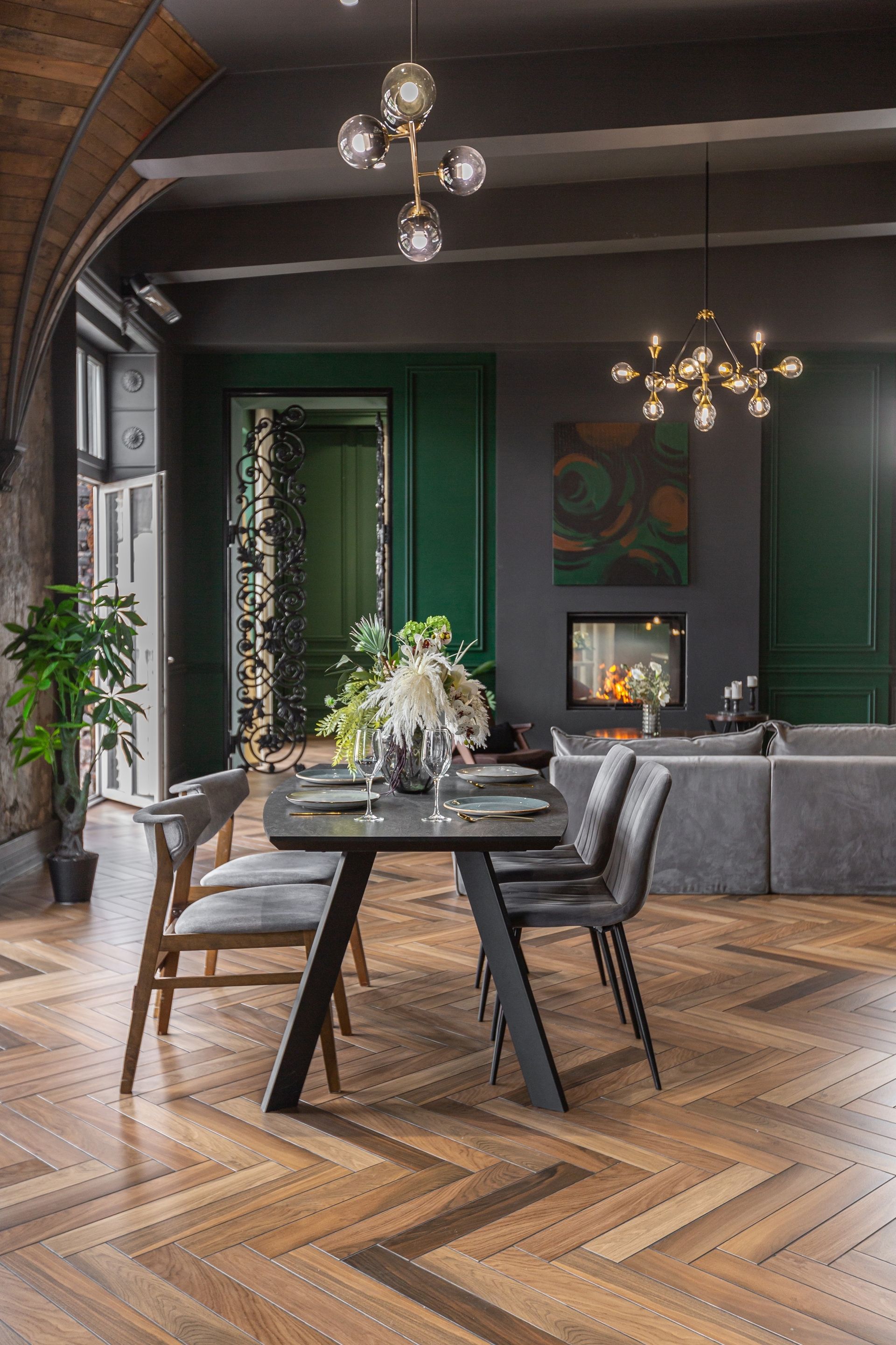 Modern dining room with a dark table, gray chairs, herringbone wood floor, and hanging pendant lights