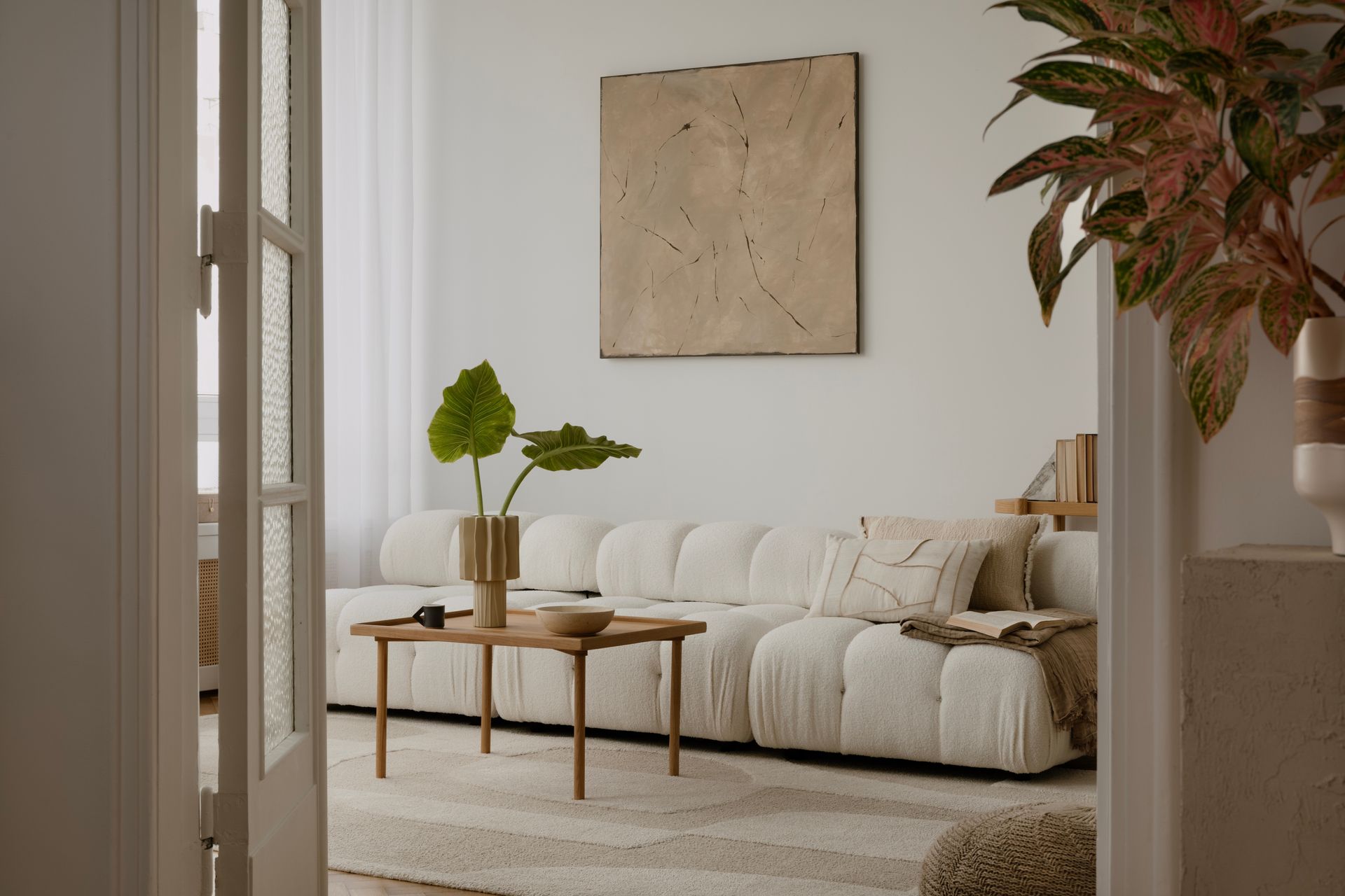 Bright living room with cream sofa, wooden coffee table, plant, and abstract wall art