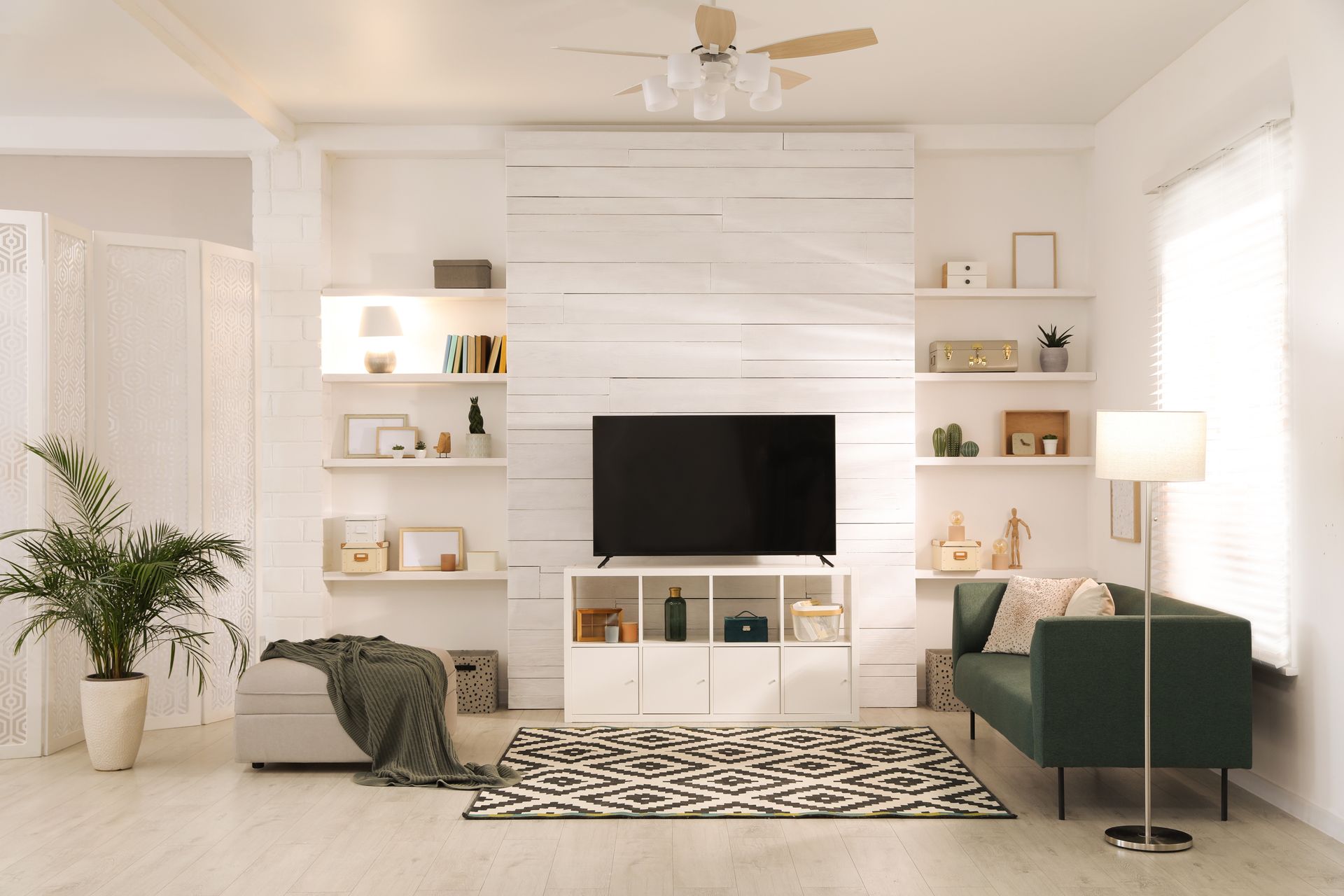Bright, minimalist living room with white walls, green sofas, a TV, and a black-and-white rug