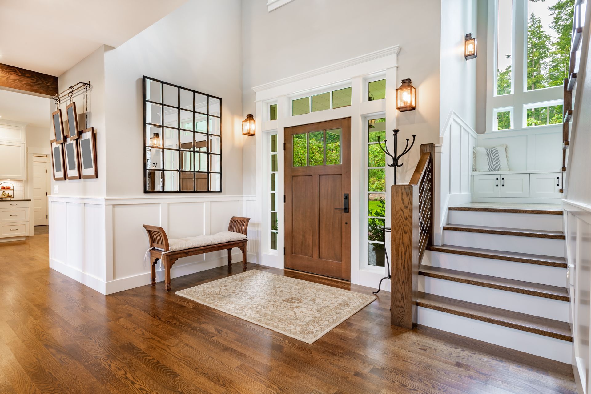 Bright entryway with wooden front door, bench, mirror, and stairs leading to an upper level