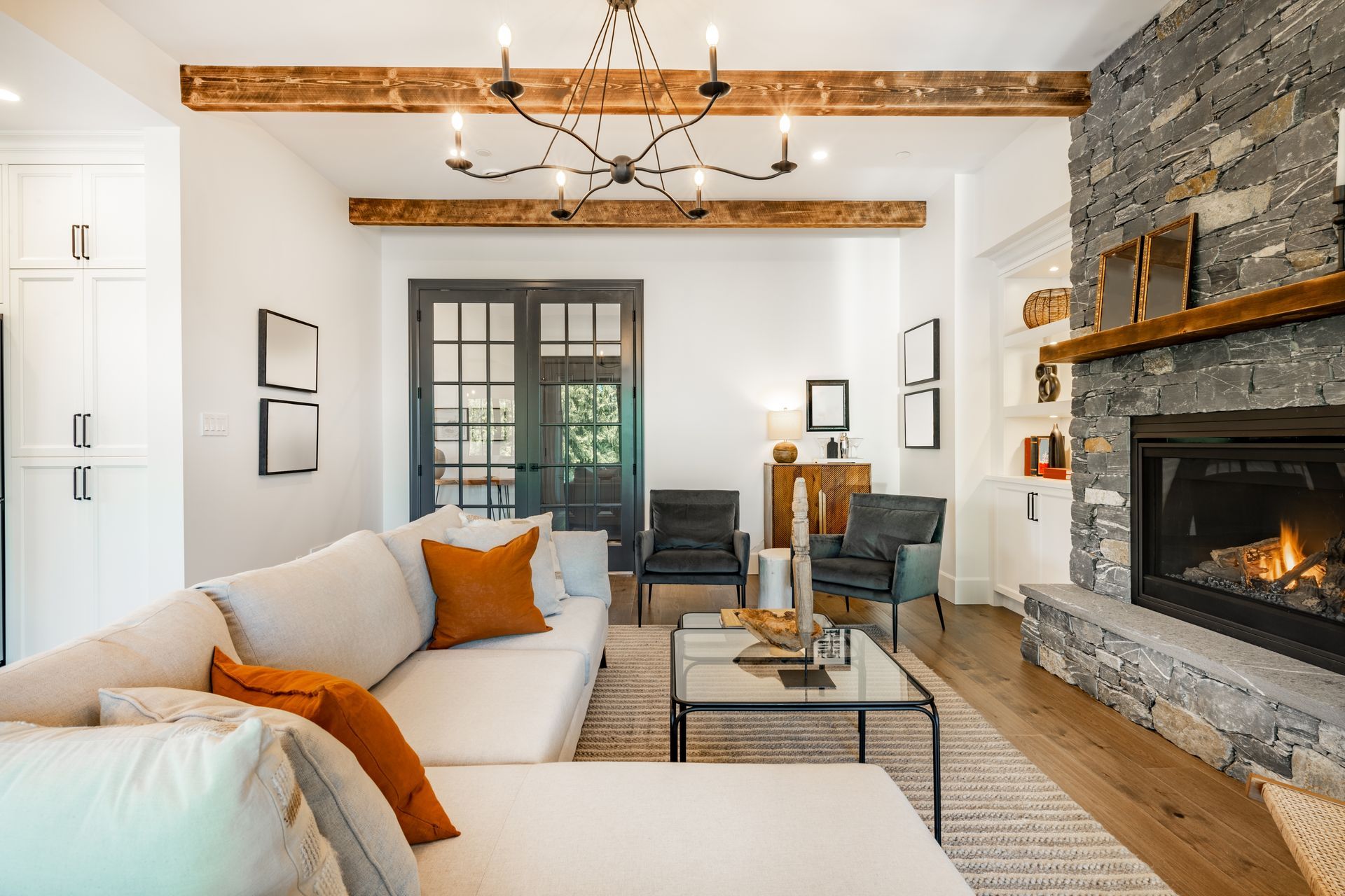 Modern living room with white sofa, stone fireplace, wood beams, and dining area in the background