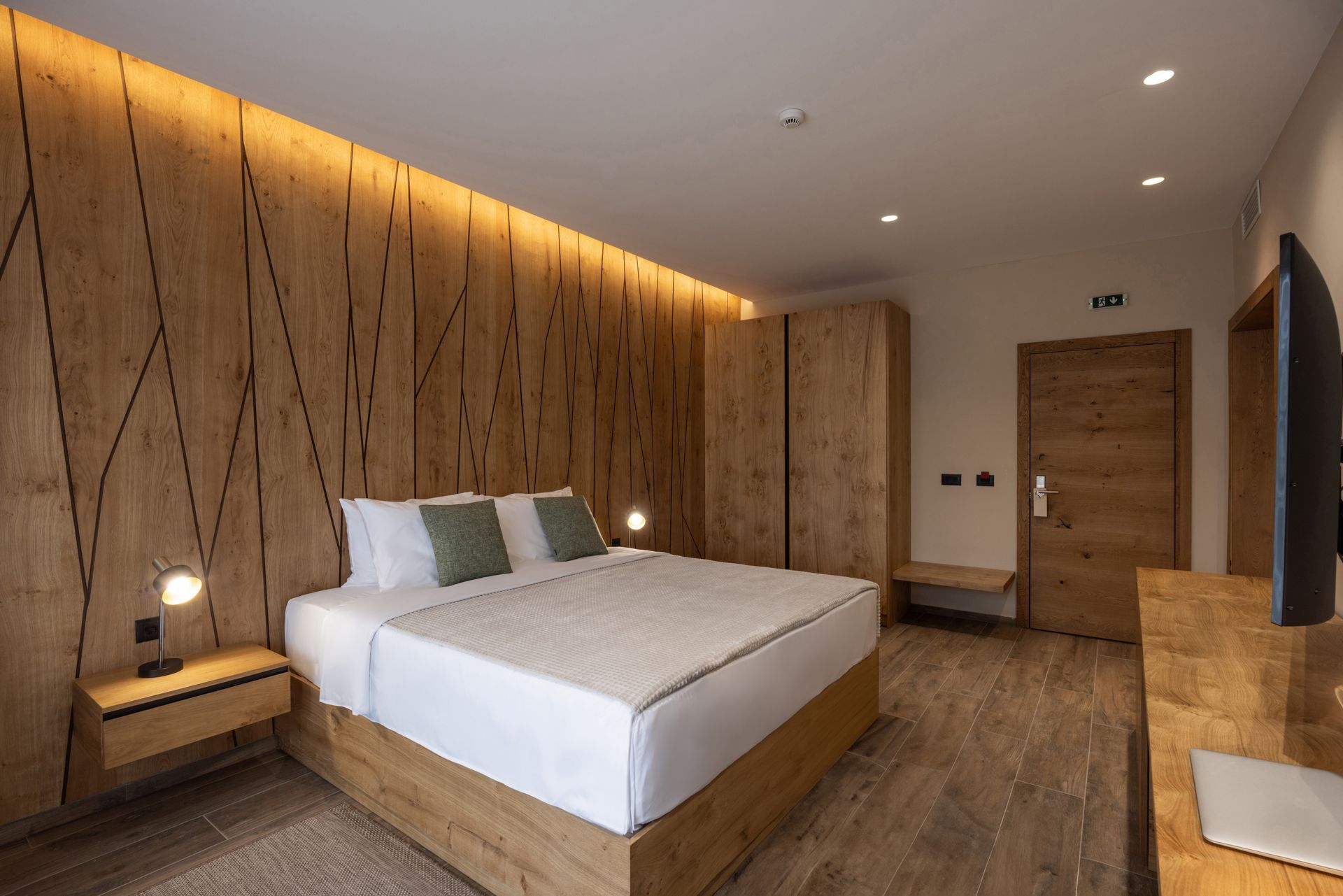 Modern hotel bedroom with a wooden accent wall, king bed, and warm recessed lighting
