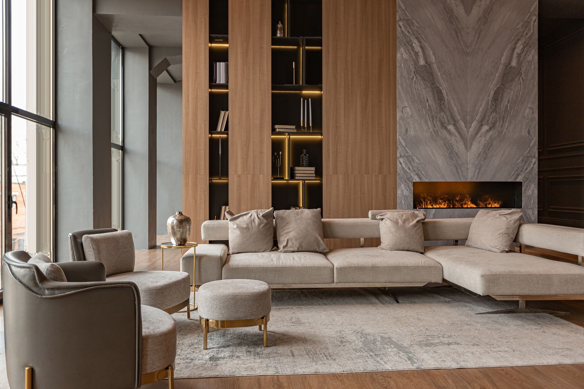 Modern living room with beige sectional sofa, marble fireplace, built-in shelves, and floor-to-ceiling windows