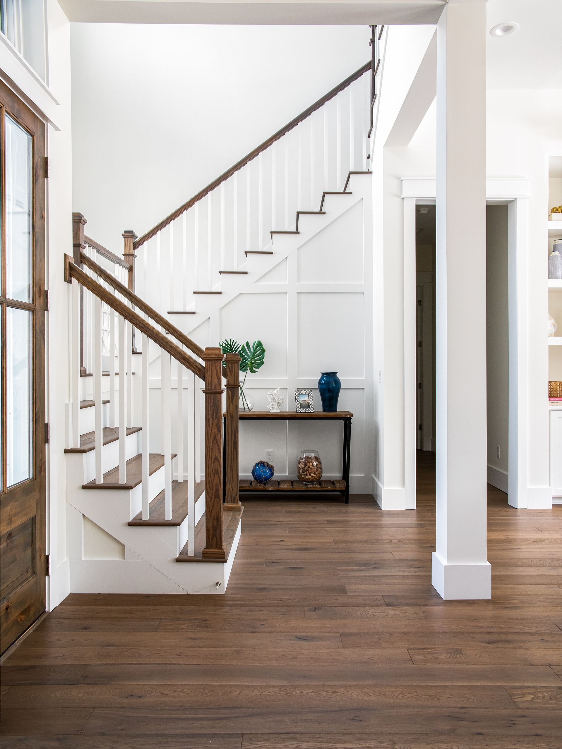 Bright foyer with wooden staircase, dark hardwood floors, and a small console table against a white wall