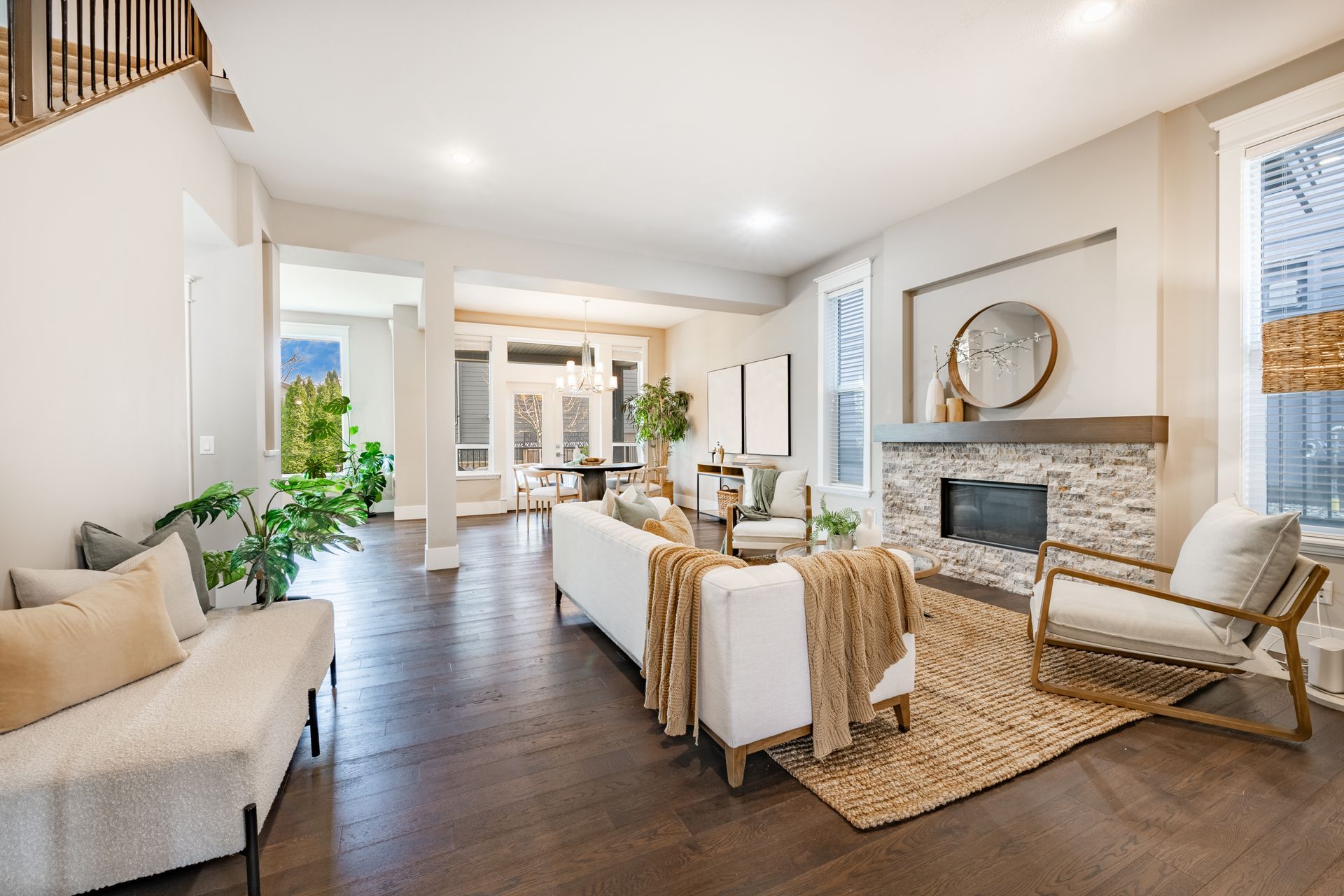 Bright living room with beige seating, dark wood floors, and a fireplace with a round mirror.