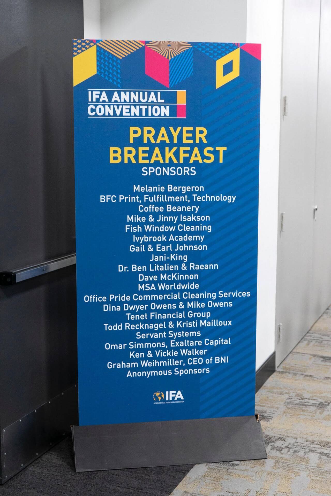 Sign for IF&A Annual Convention Prayer Breakfast with sponsor names, in front of a hallway.
