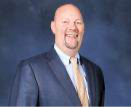 Smiling man in a suit with a gold tie, on a blue background.