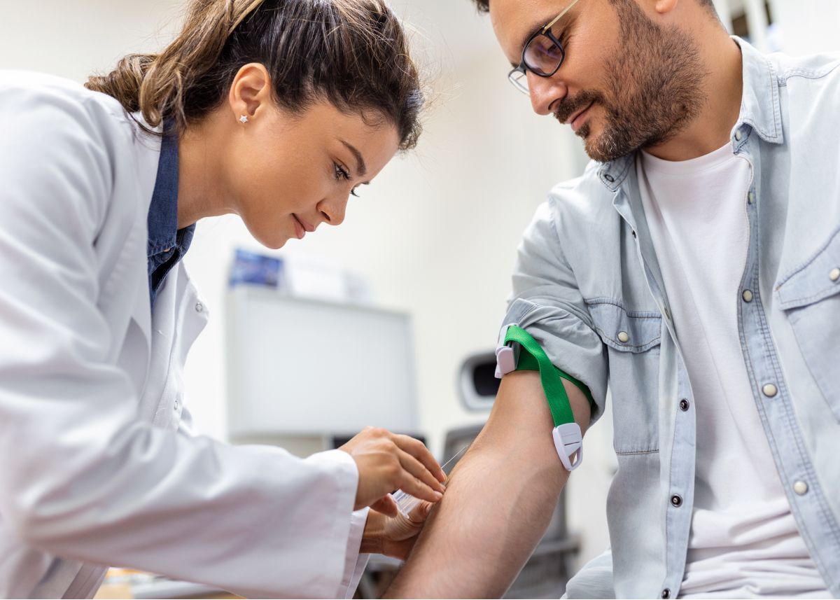 Profissional de saúde coletando sangue de um paciente em uma clínica, utilizando um torniquete verde.