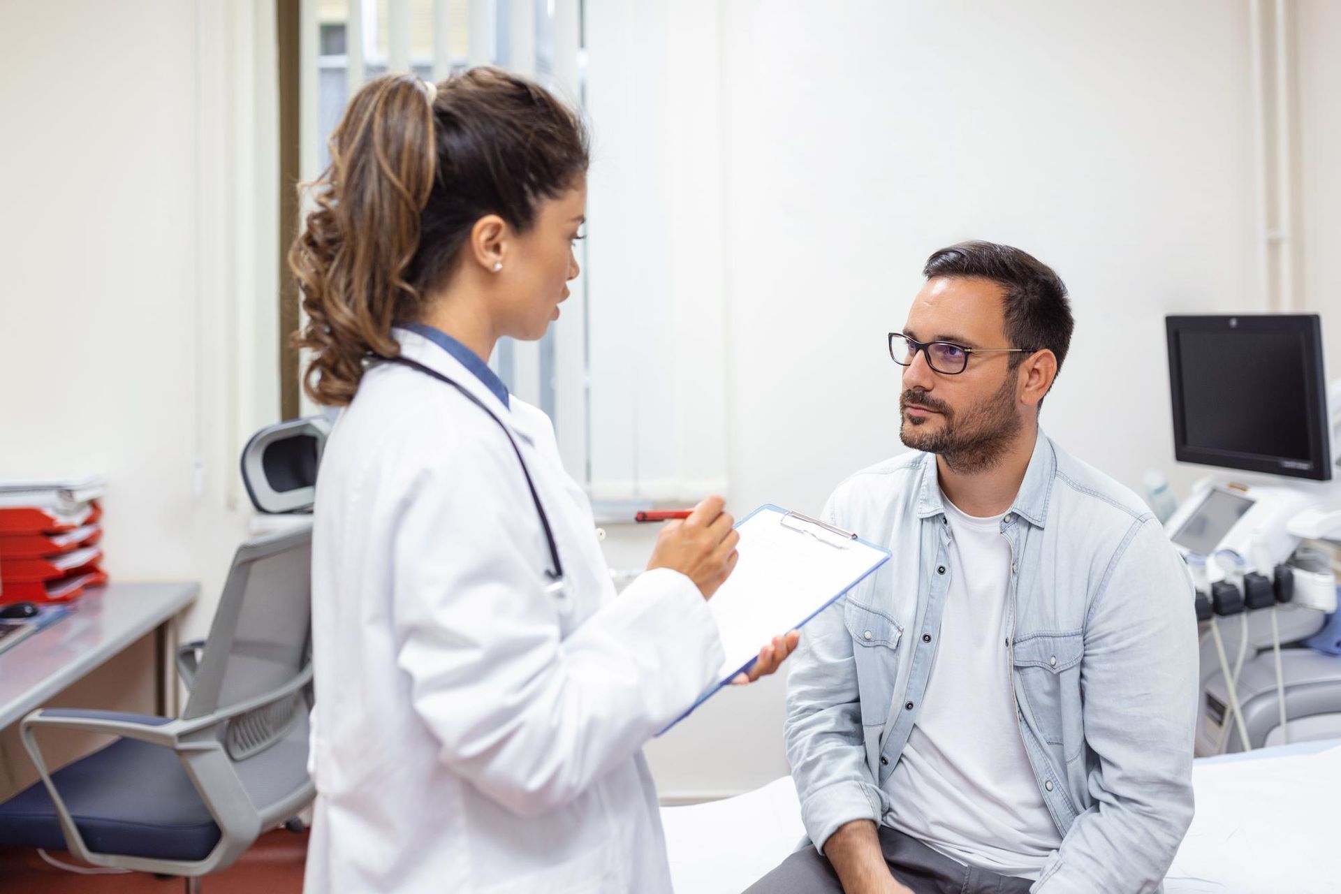 Médico atendendo um paciente sentado em um consultório bem iluminado, fazendo anotações em uma prancheta.