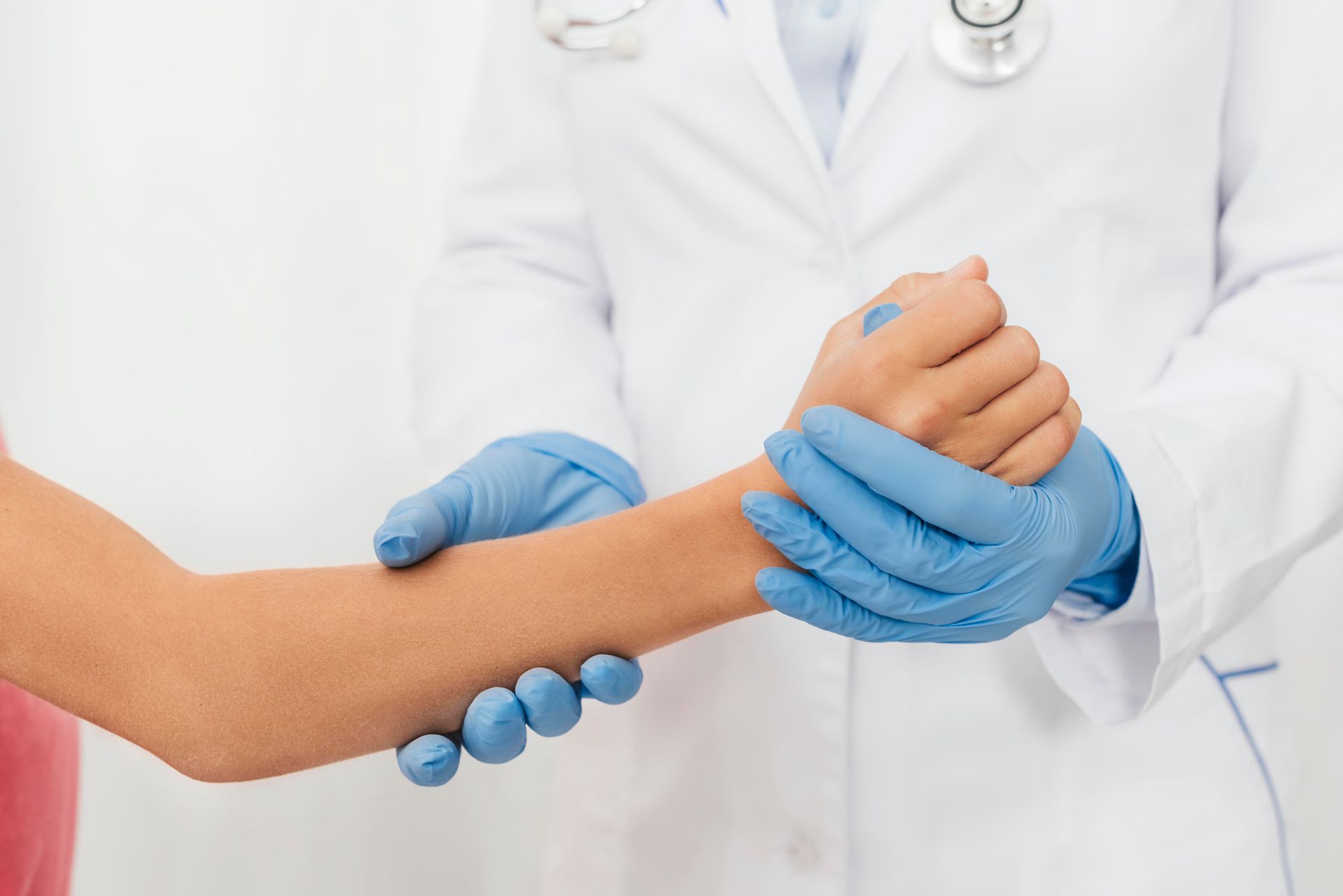 Médico de jaleco branco e luvas azuis segurando o pulso de um paciente durante um exame.