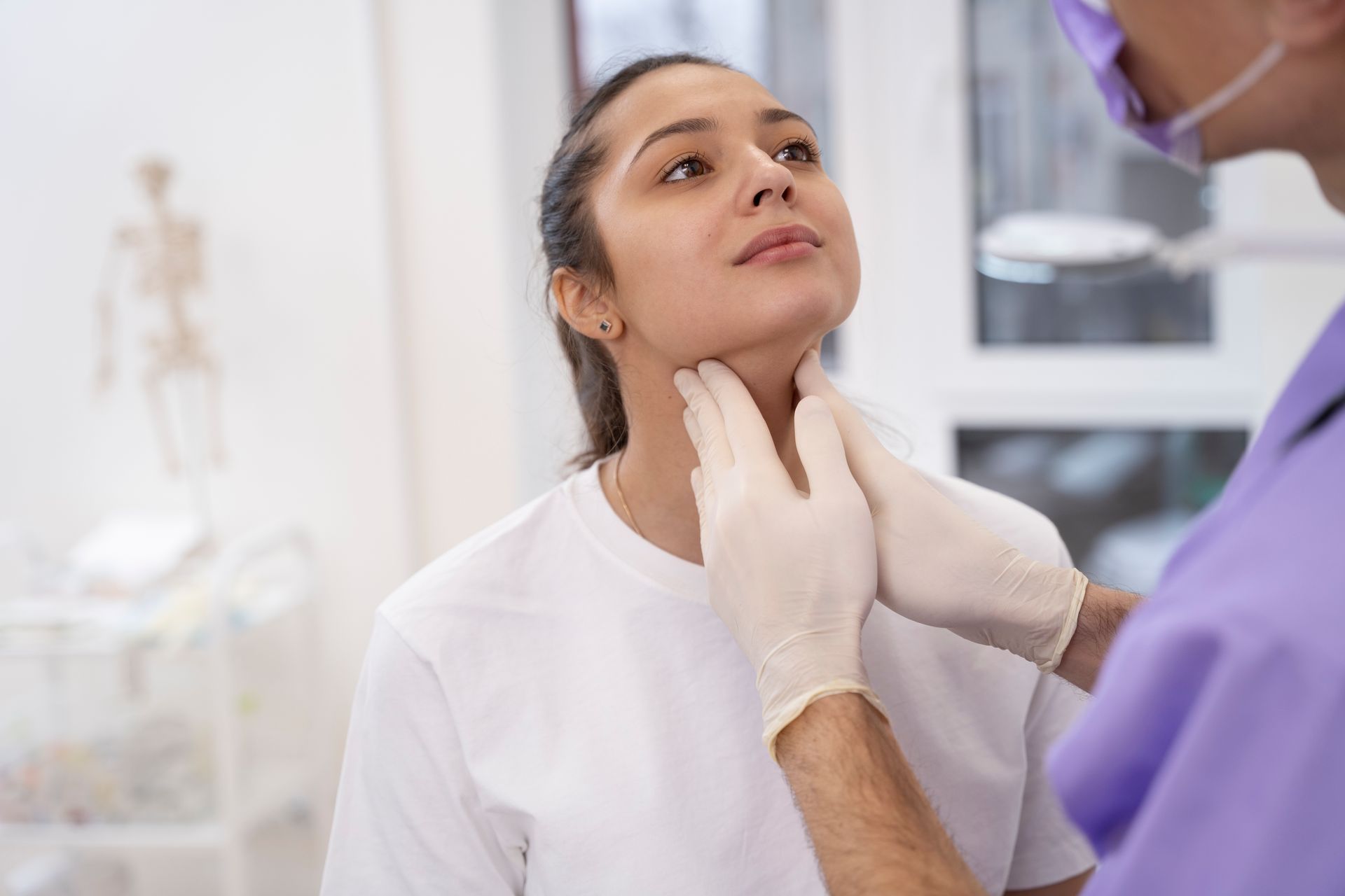 Profissional de saúde examinando o pescoço de um paciente em uma clínica, com o paciente sentado ereto.