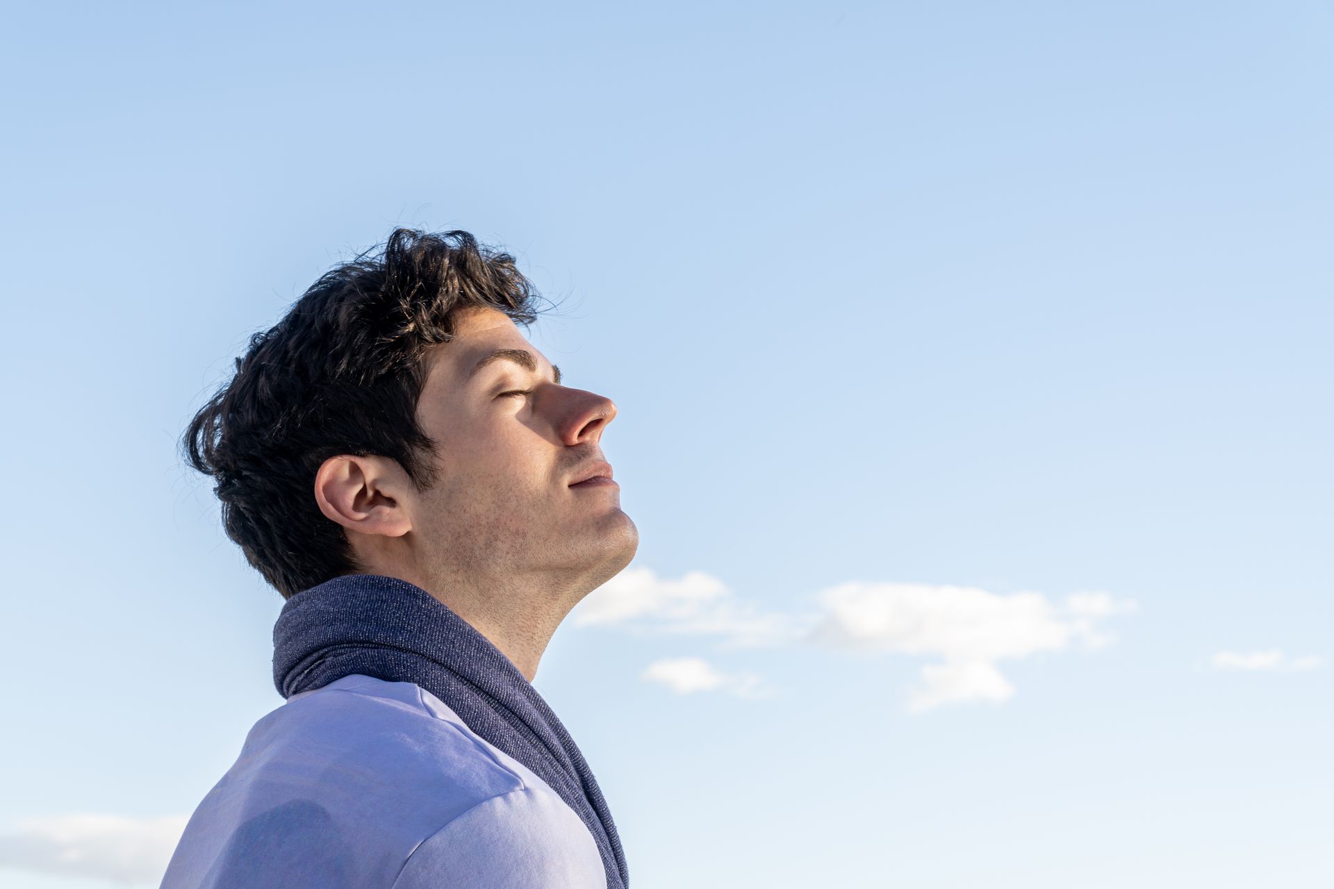 Pessoa de perfil com os olhos fechados, usando um cachecol contra um céu azul claro.