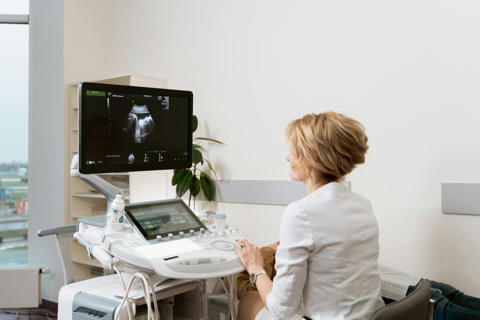 Pessoa utilizando um aparelho de ultrassom em uma sala de clínica bem iluminada, visualizando uma imagem fetal no monitor.