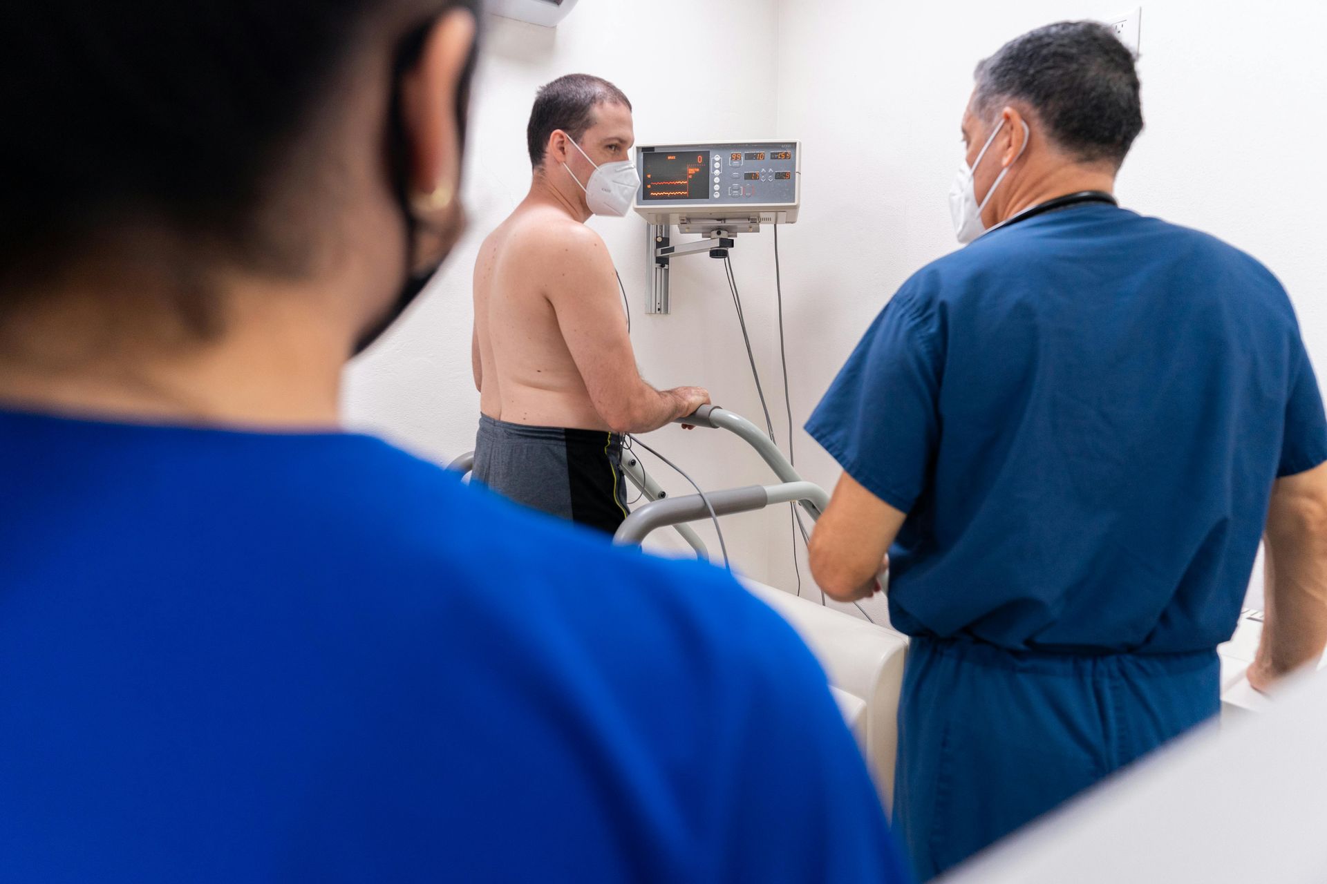 Equipe médica examinando um paciente em uma sala de clínica, com um monitor e equipamento de soro por perto.