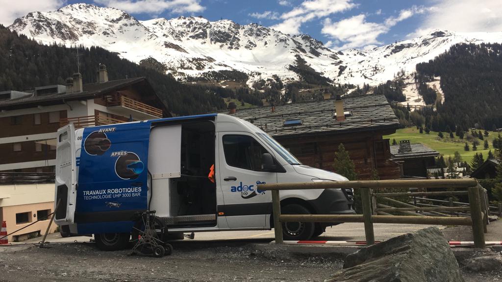 Une camionnette bleue et blanche est garée devant une montagne enneigée.
