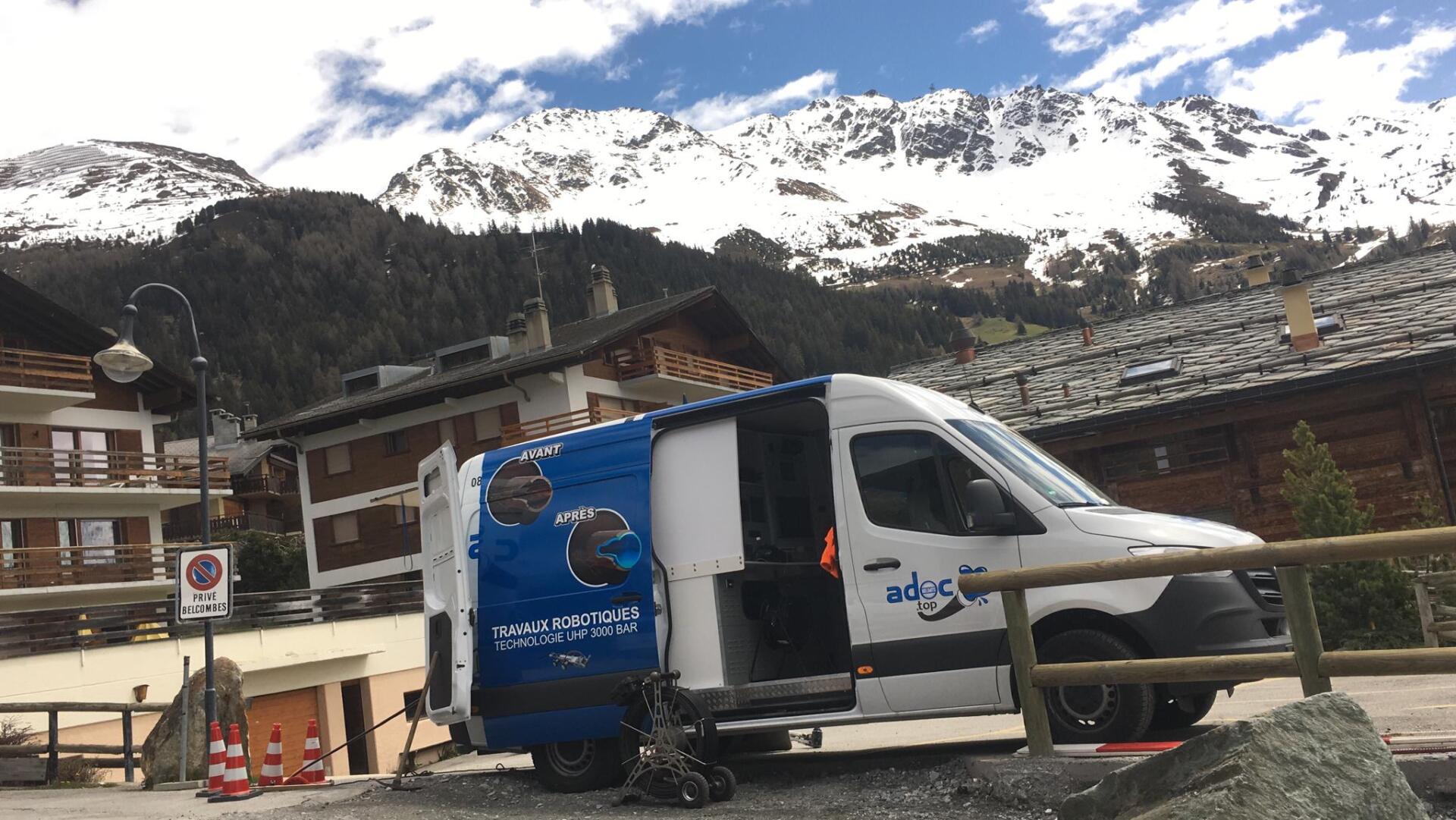 Une camionnette bleue et blanche est garée devant une montagne enneigée.
