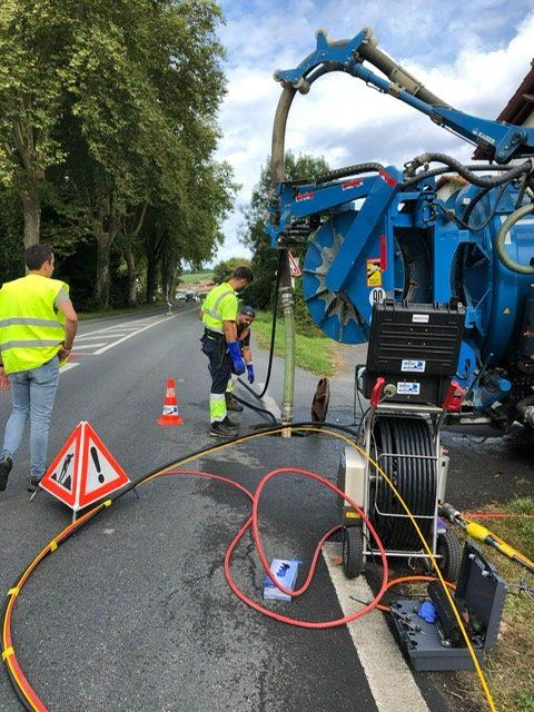 Un homme en gilet jaune se tient à côté d'un camion aspirateur sur le bord de la route.