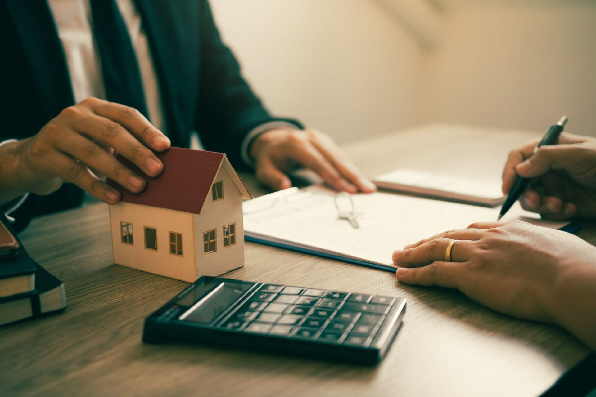Hands and house model on a desk with calculator and paperwork during a meeting