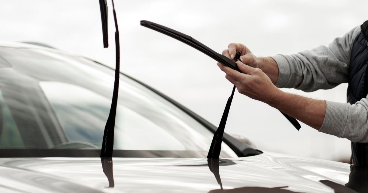 Person replacing a windshield wiper on a car; cloudy day.