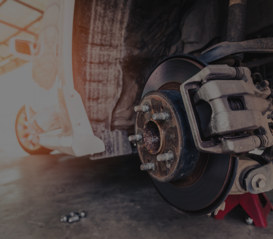 Car wheel removed, brake disc exposed, supported by jack stands in a garage.