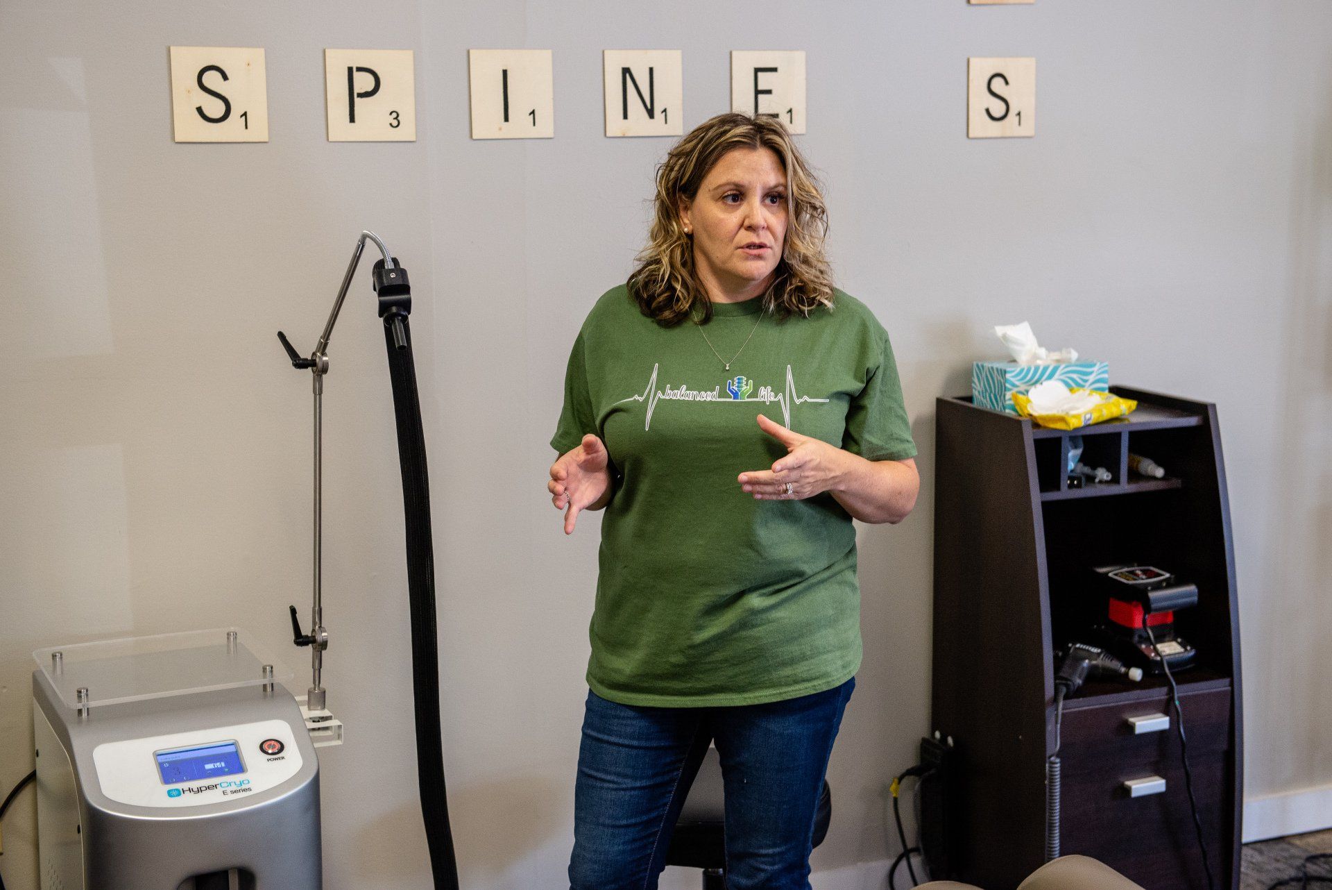 A woman in a green shirt is standing in a room with scrabble tiles on the wall.