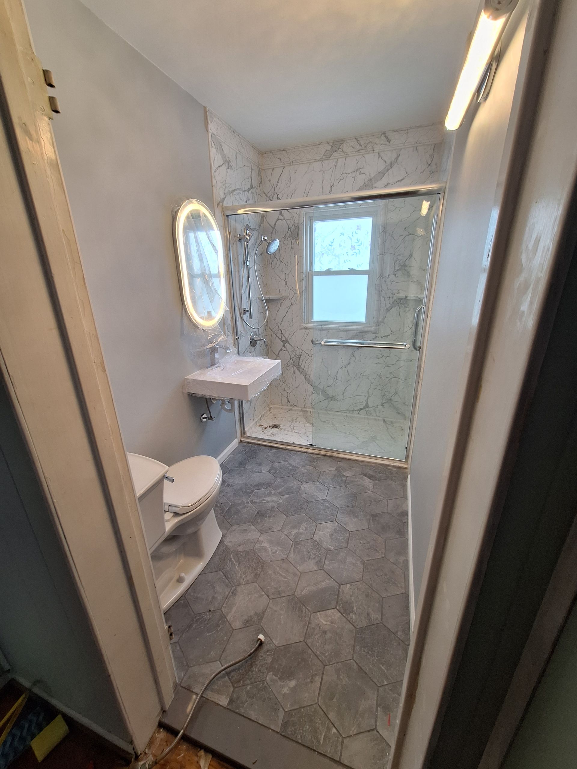 Small tiled bathroom with toilet, sink, oval mirror, and frosted glass shower door.