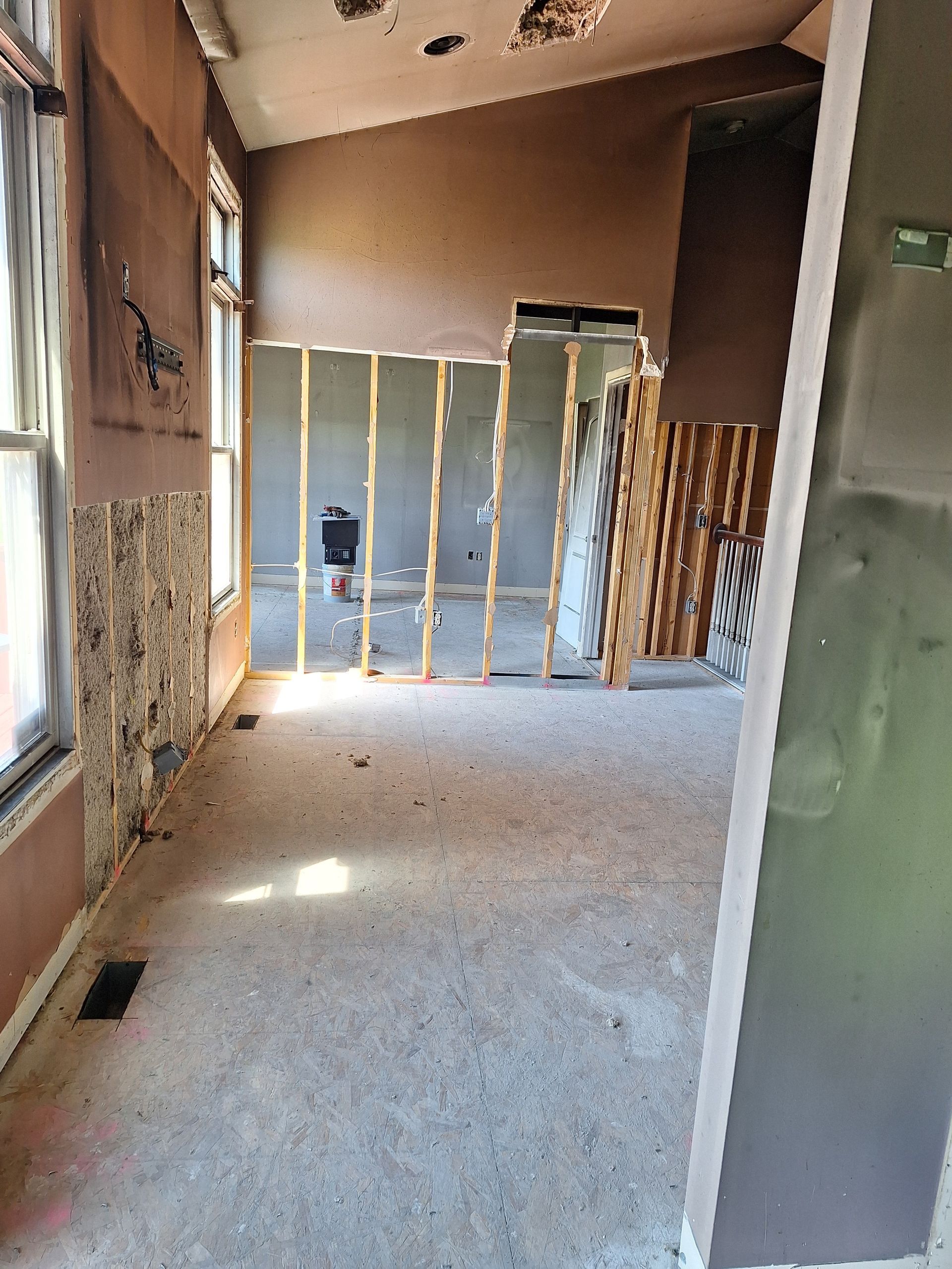 Empty unfinished room with exposed wall framing, beige carpet, and a window on the left.
