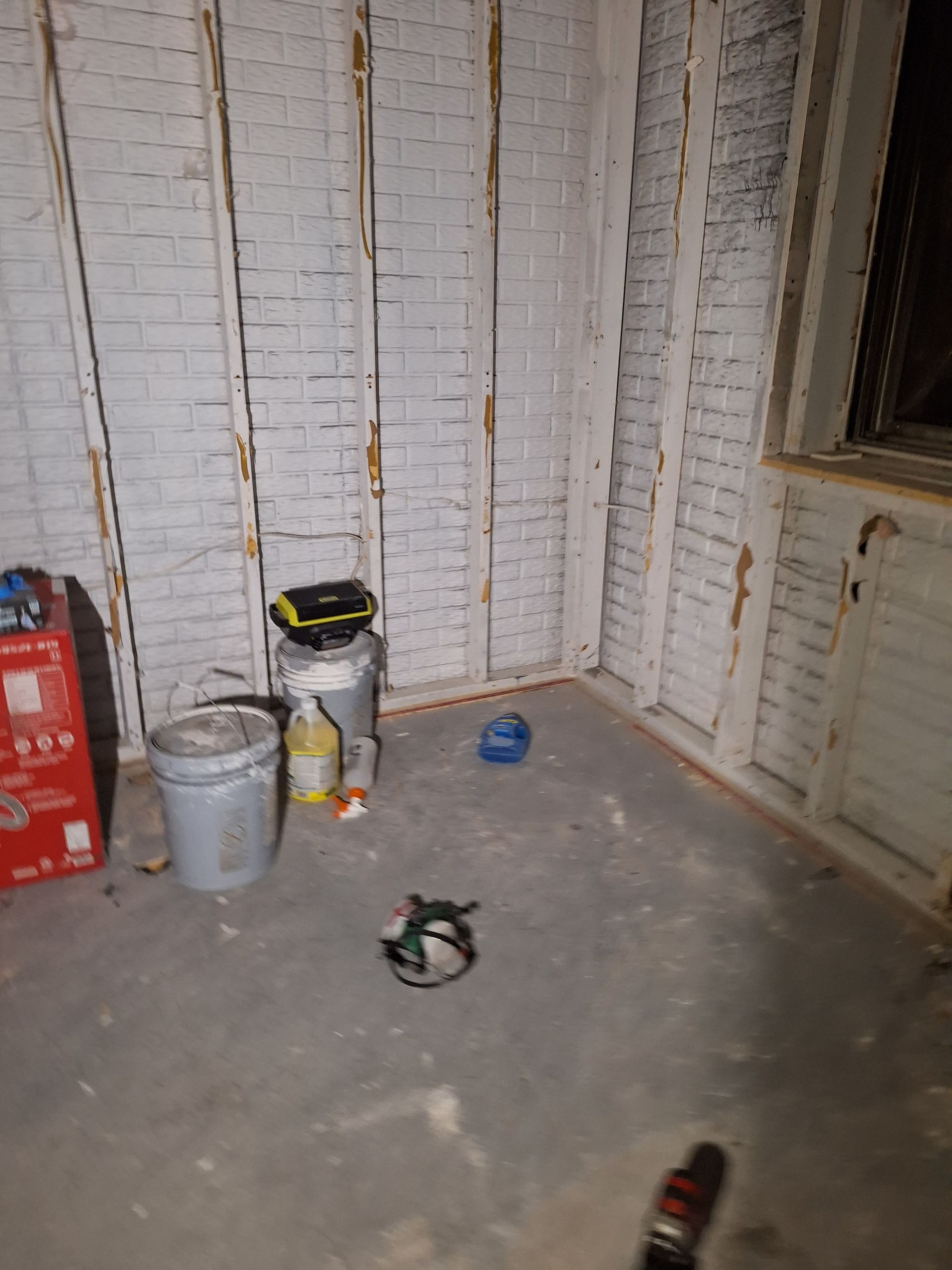 Bare room with exposed brick walls, a bucket and paint can on the floor, and scattered tools.