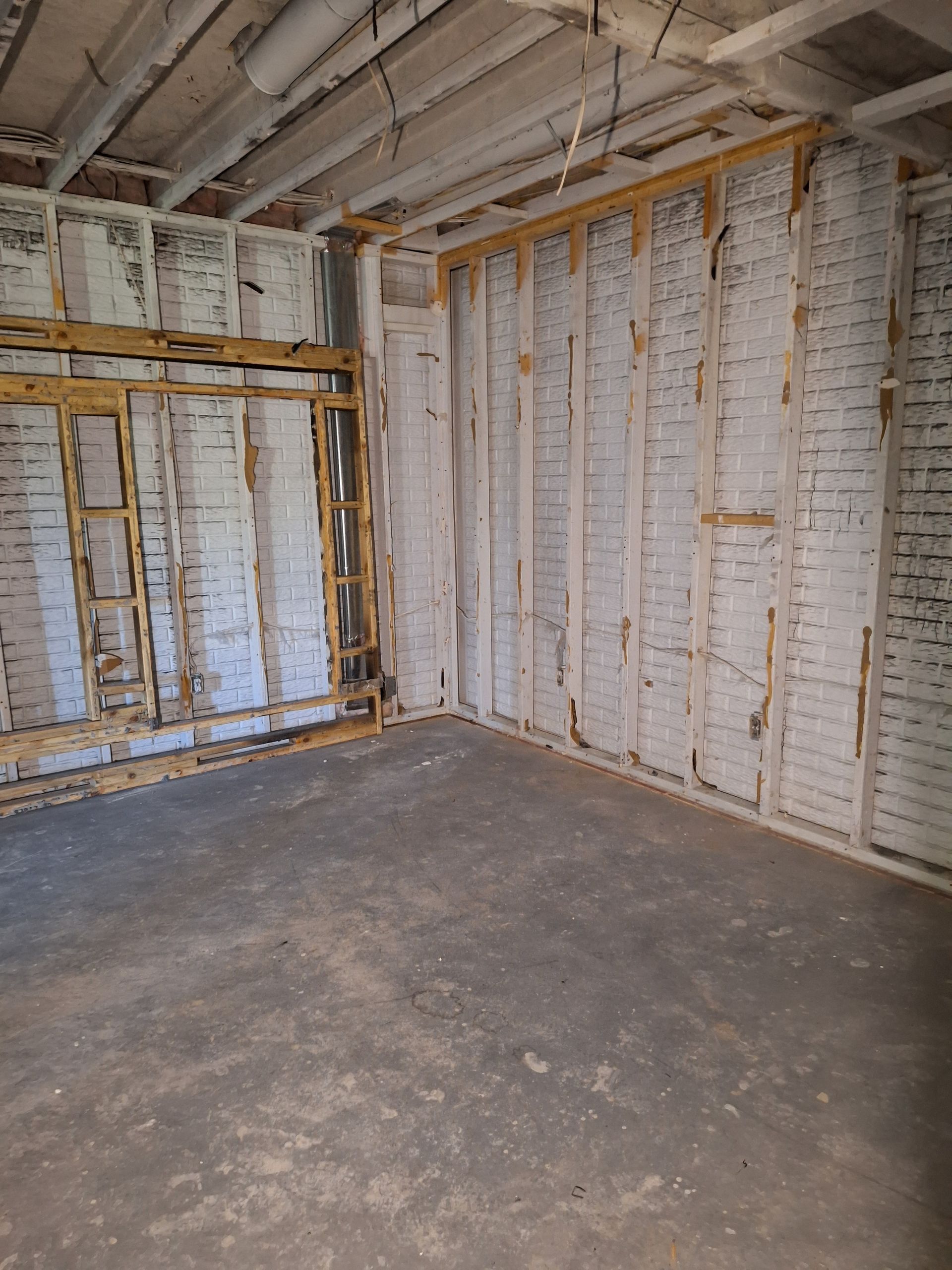 Empty unfinished room with exposed white insulation, wooden framing, and a bare concrete floor.