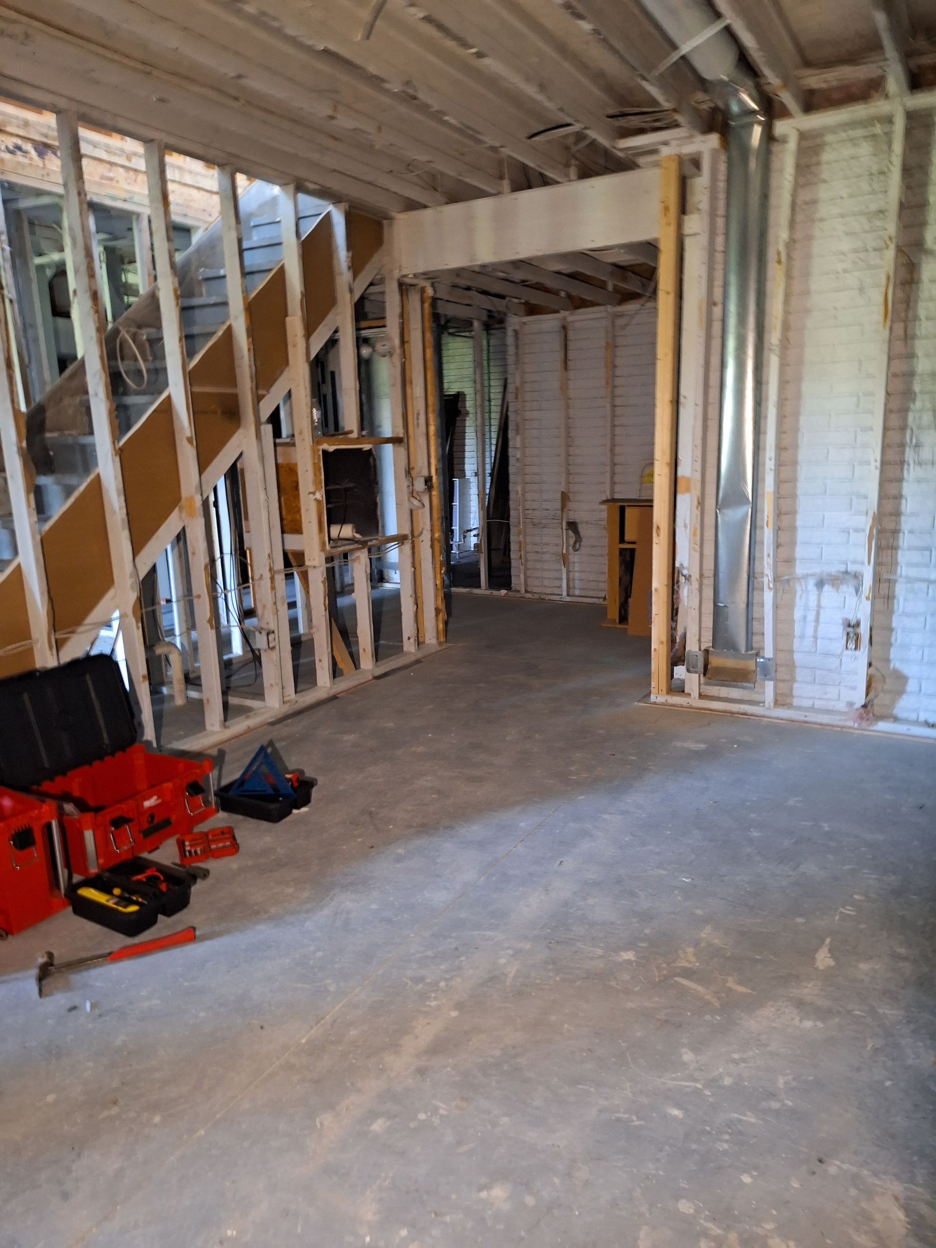 Unfinished room with exposed framing, open doorway, bare subfloor, and tools on the floor.