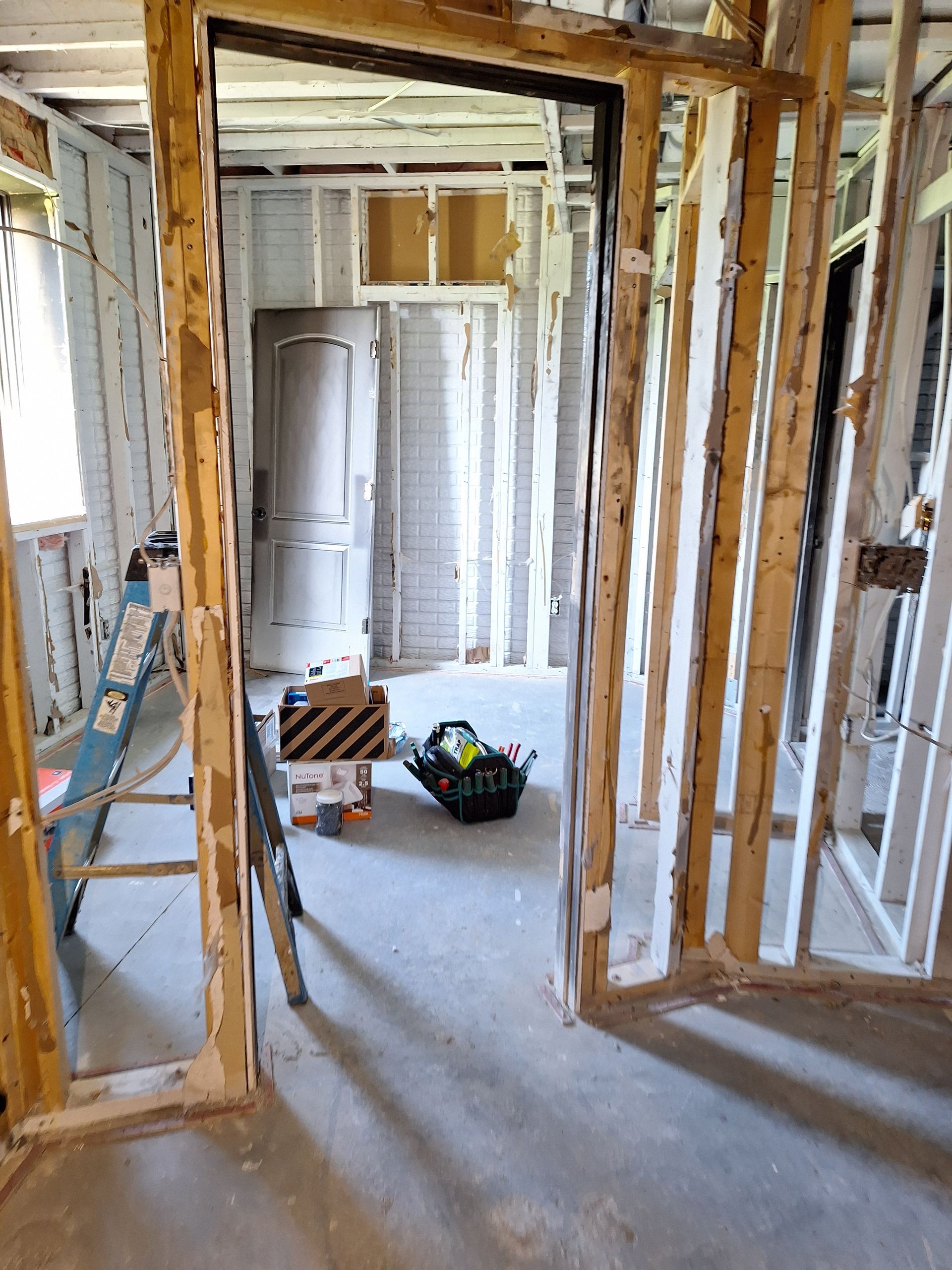 Framed interior under renovation with exposed studs, drywall, and tools on the floor