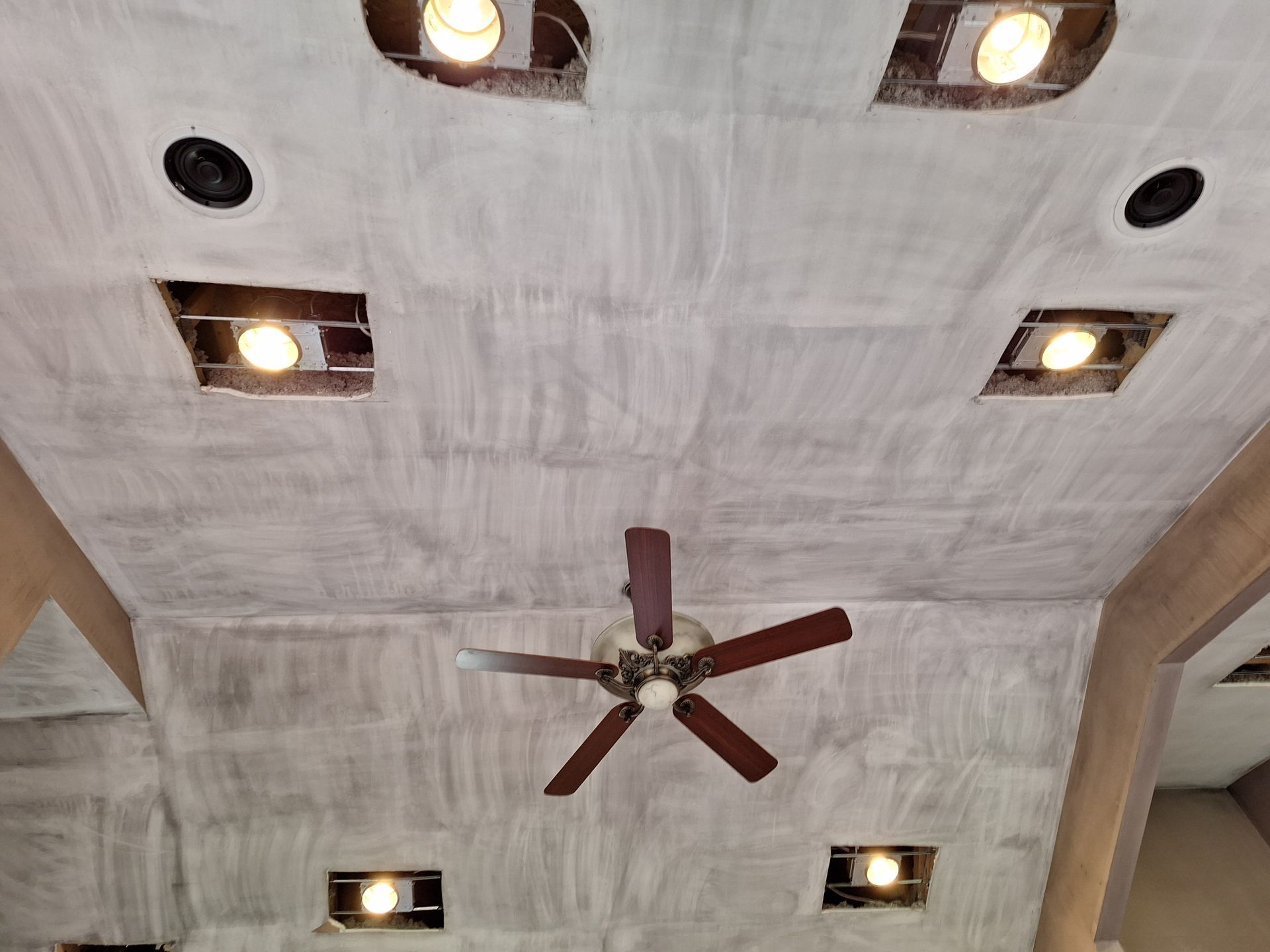 Ceiling with recessed lights and a central ceiling fan on a textured white surface