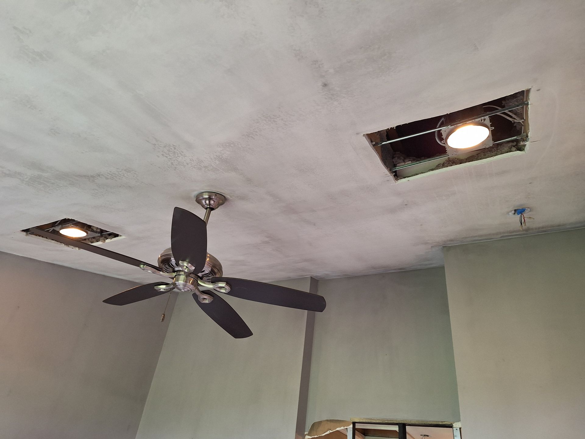 Ceiling with a black ceiling fan and two recessed lights in a gray room.