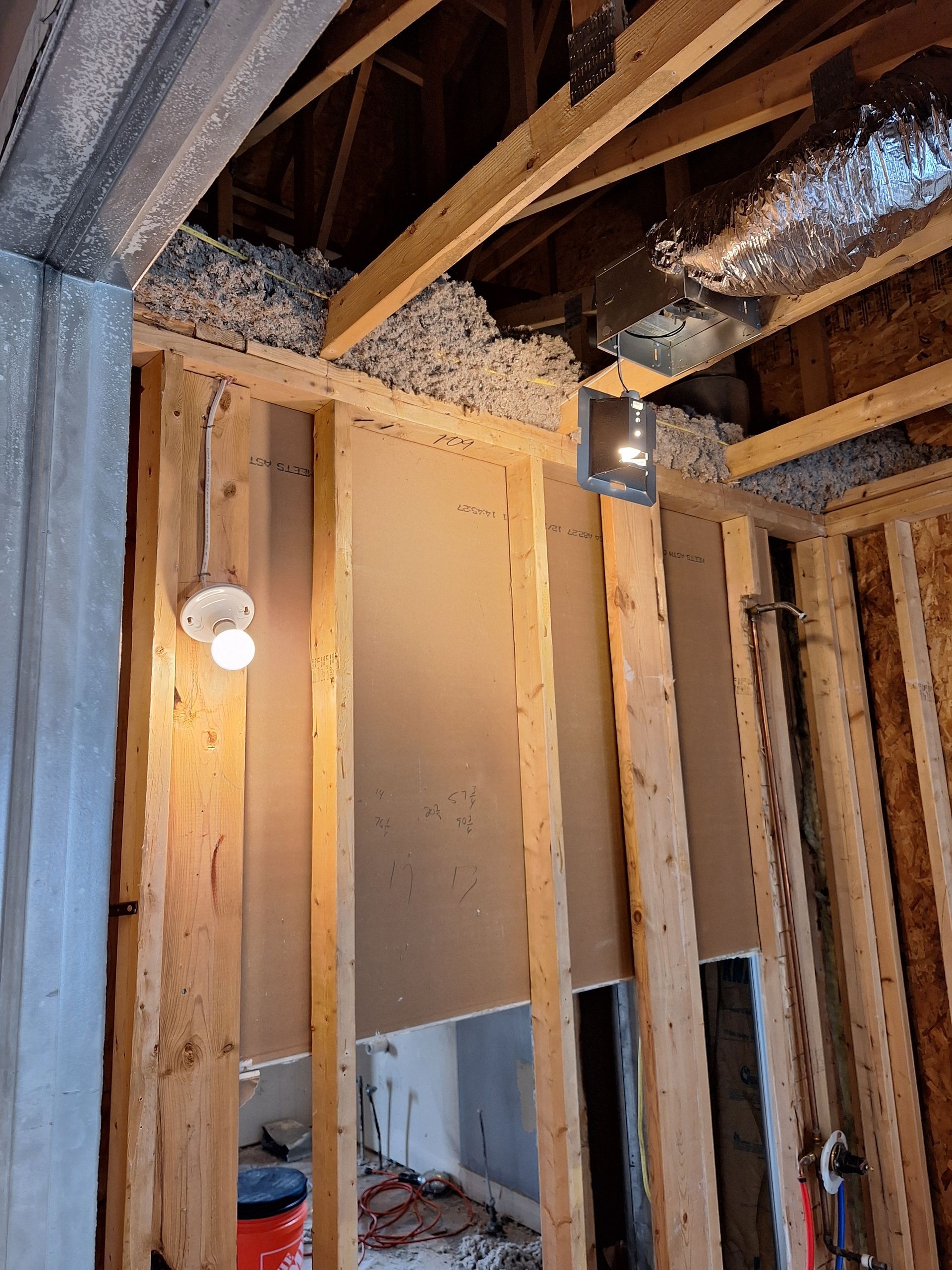 Unfinished interior wall framing with exposed studs, insulation, and a hanging light bulb.