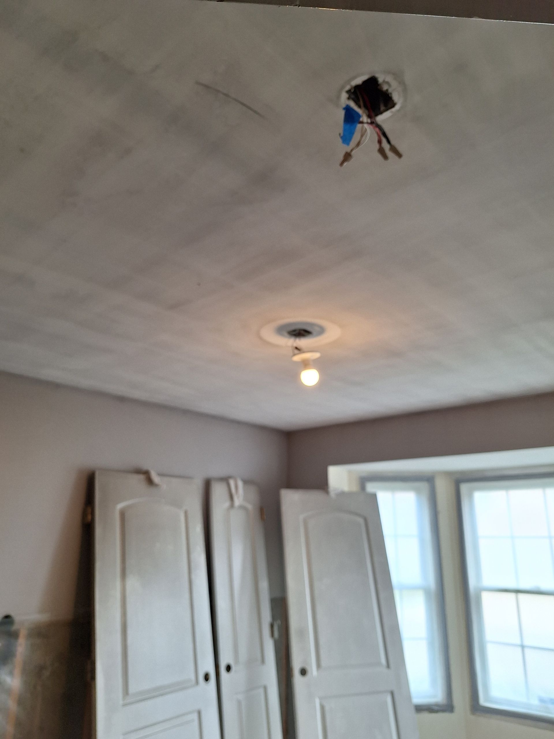 Ceiling with dangling light fixture wires above white wardrobe doors and a bright window.