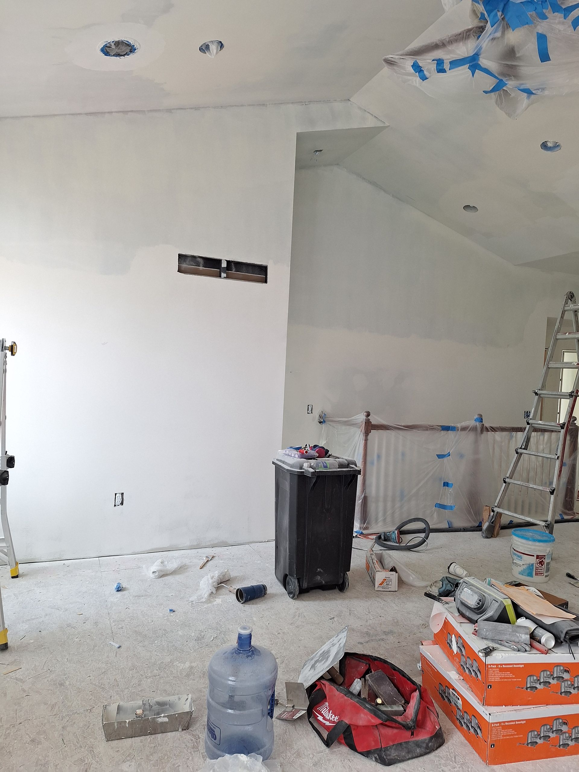 Partially renovated room with white walls, tools, debris, and construction materials scattered on the floor.