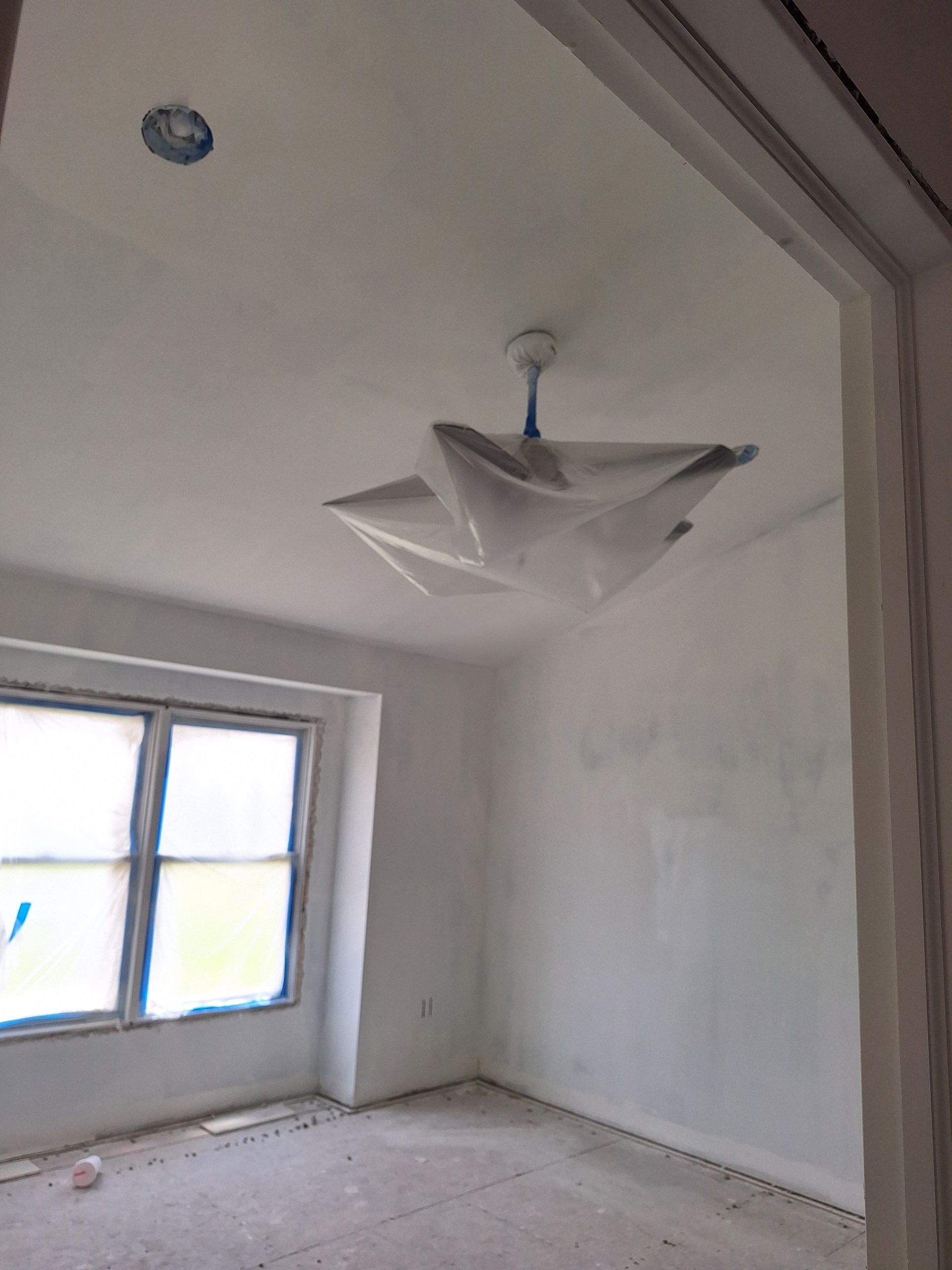 Empty white room with a window and a hanging light fixture, covered by a plastic sheet