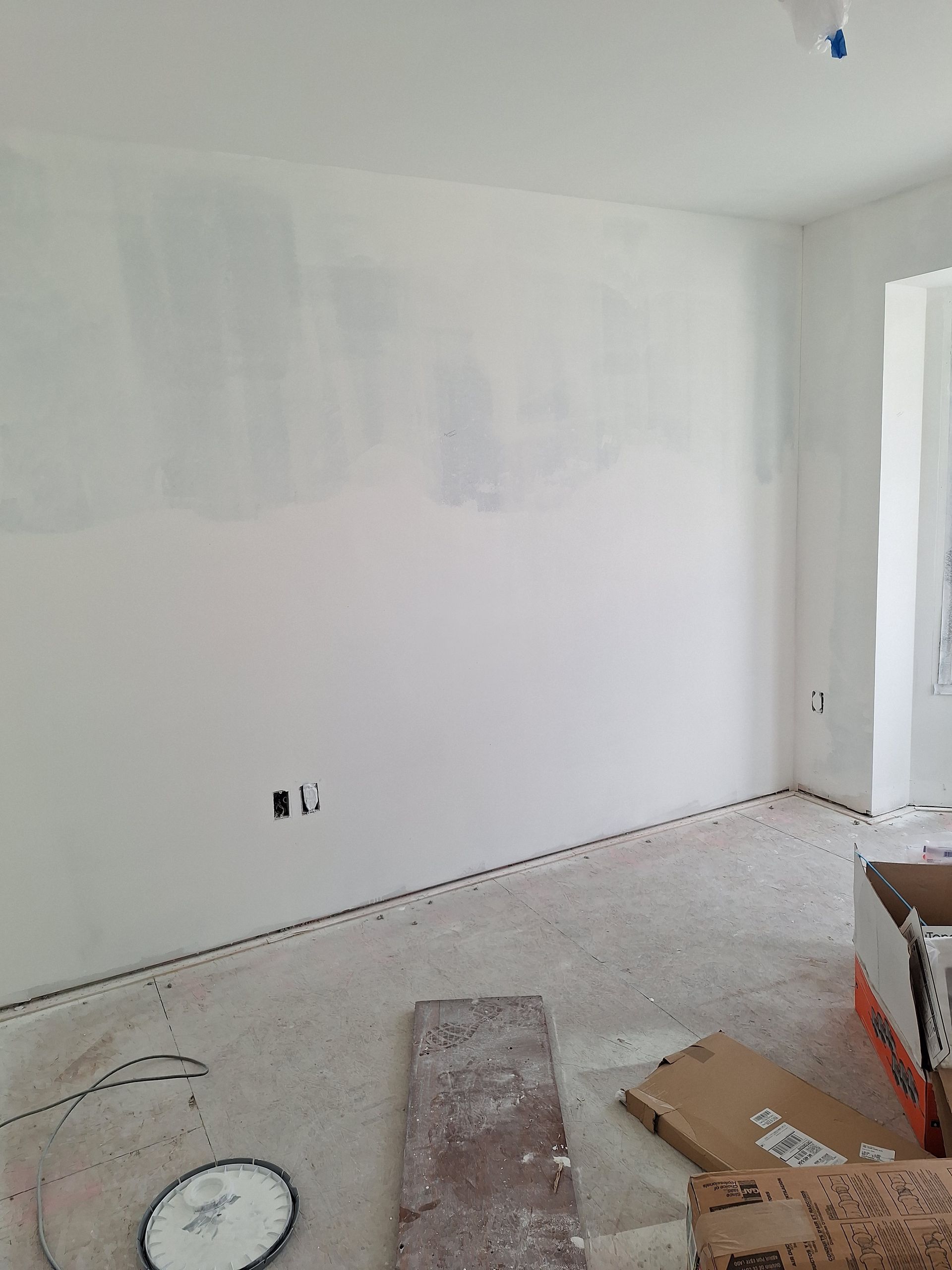 Partially painted white room with tools and supplies on the floor