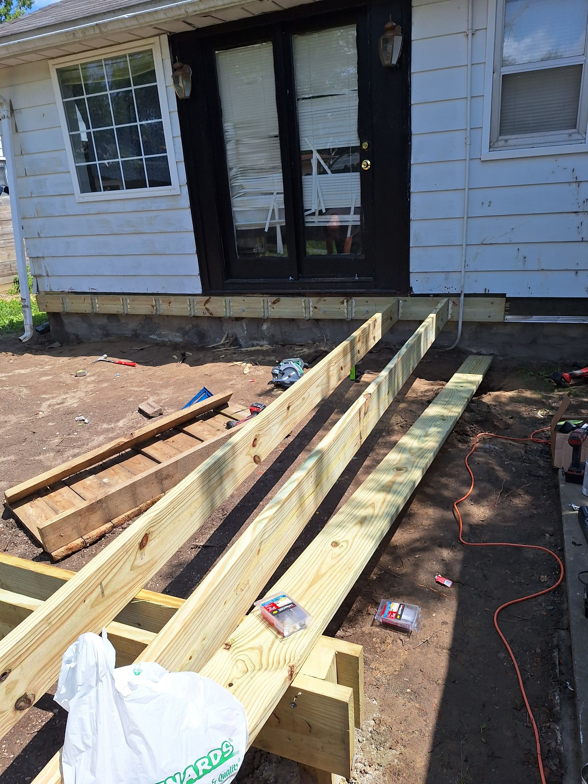 Front porch construction with wooden ramp framing beside a gray house, tools and lumber on dirt.