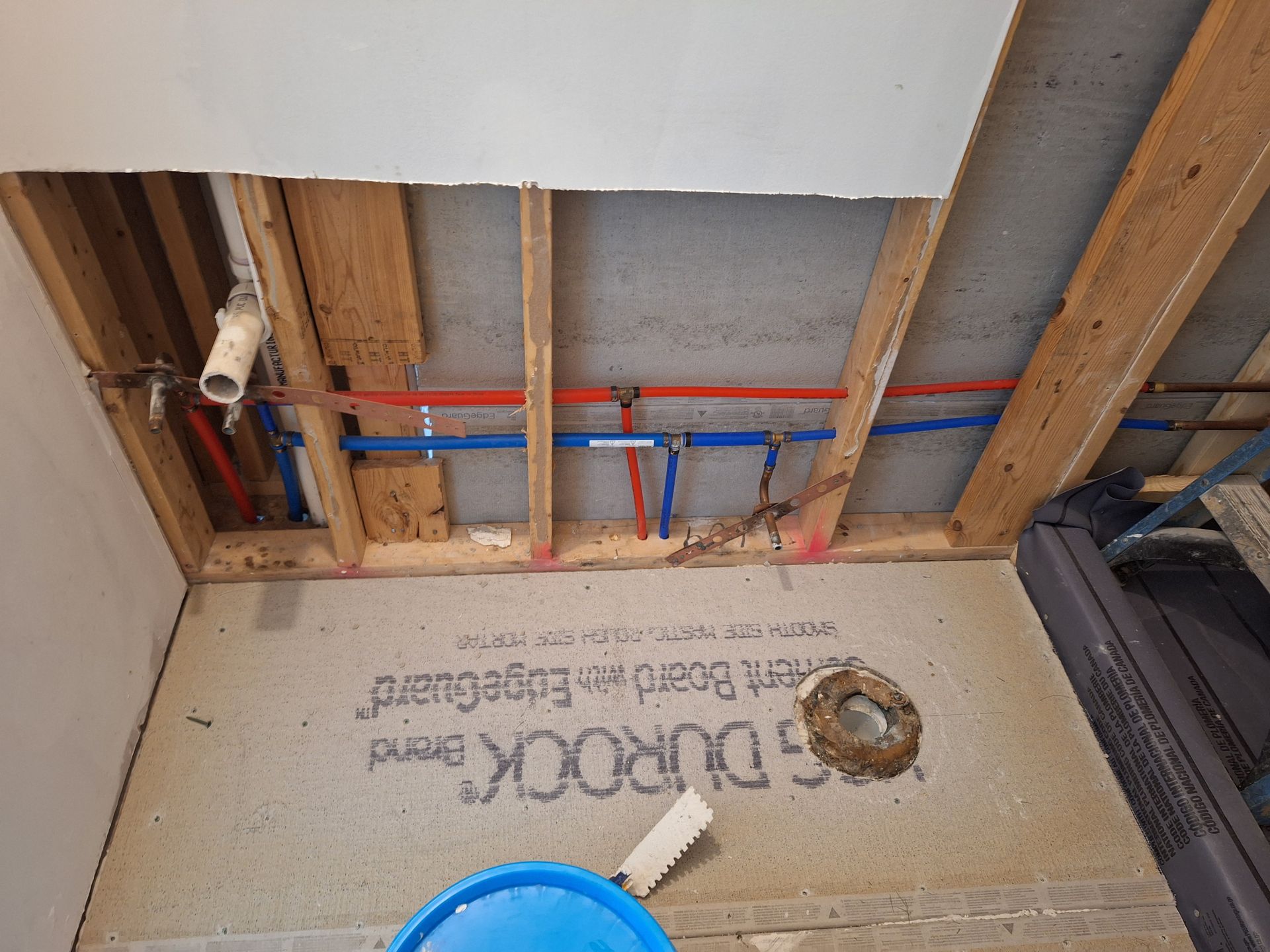 Exposed bathroom plumbing and joists above a partially removed floor, with red and blue pipes visible.