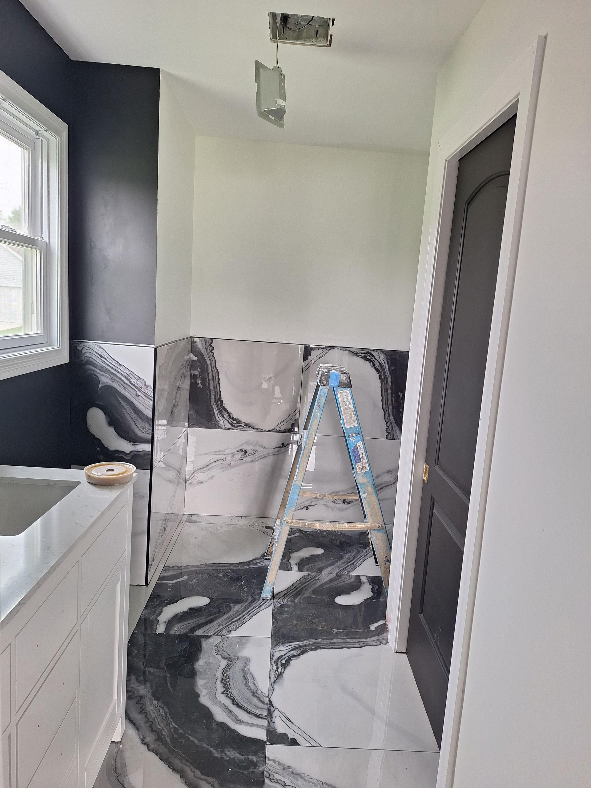 Bathroom under renovation with black-and-white tile floor, ladder, and white walls