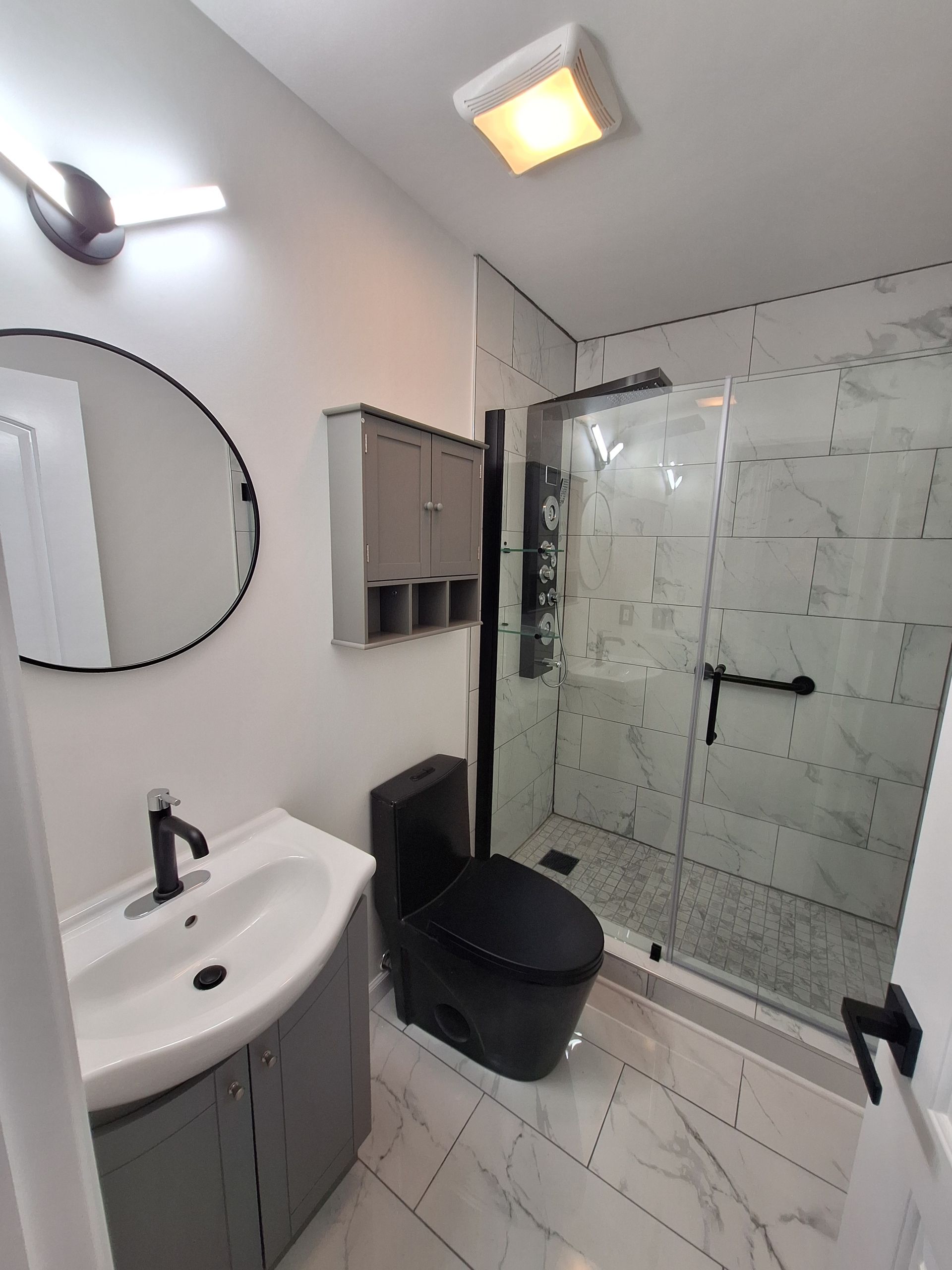 Modern bathroom with sink, toilet, glass shower, and gray tile floor and walls